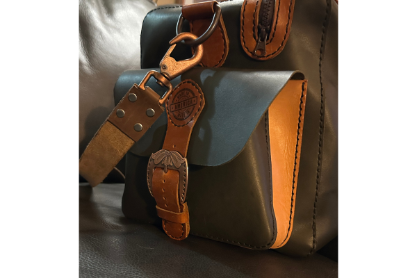 Brown leather bag with a matching strap and keychain on a white background