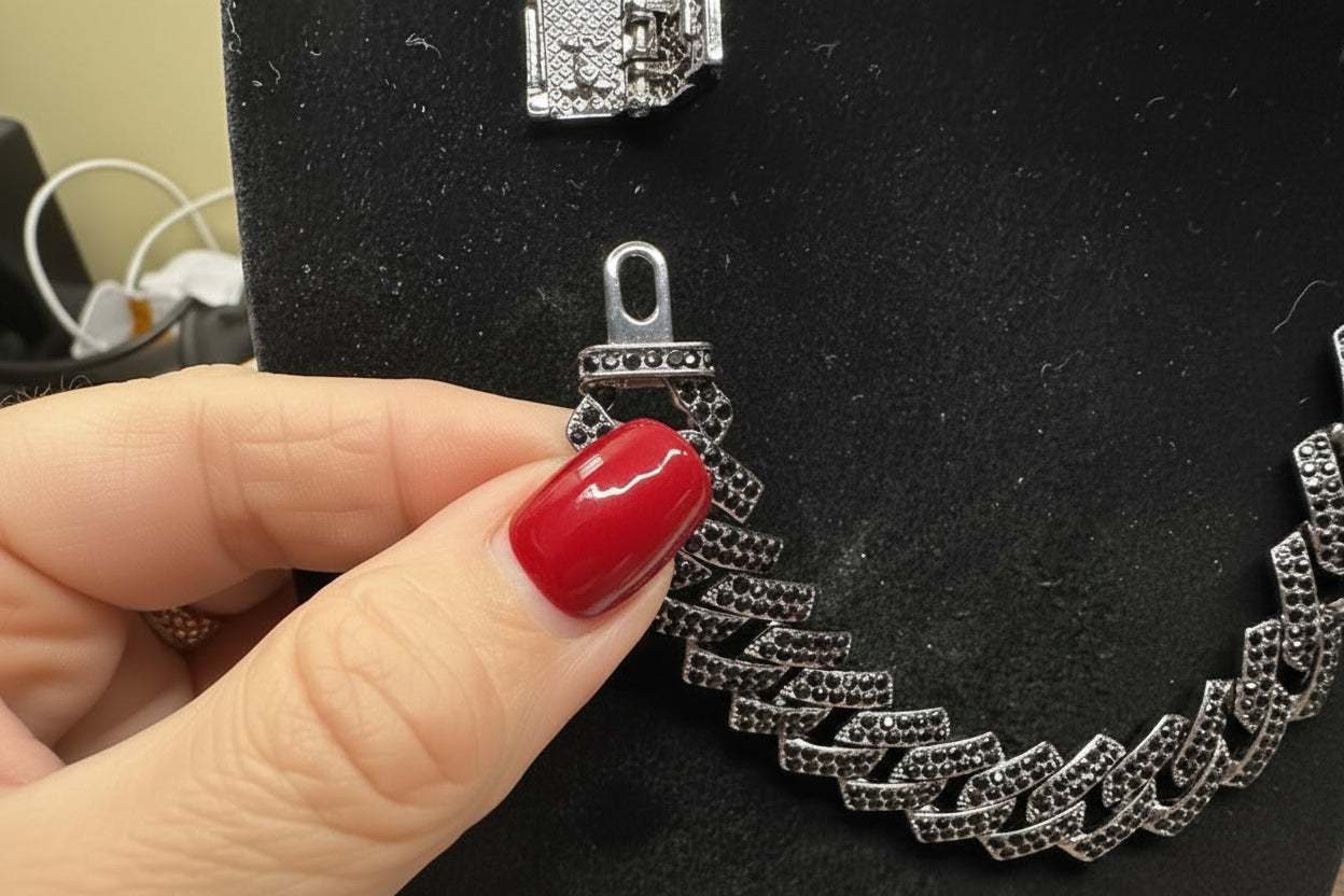 Silver bracelet on a black velvet stand with a hand holding it.