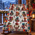 A colorful quilted blanket featuring vintage Christmas illustrations of children in bonnets, trees, snowflakes, and a 'Merry Christmas' sign, draped over a rustic wooden rocking chair in a cozy cabin setting with a snowy mountain background.
