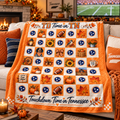 An orange and cream checkered fleece throw blanket with Tennessee football theme is draped over a couch in a cozy living room setting. The blanket features 'TD Time in TN' and 'Touchdown Time in Tennessee' text, footballs, pumpkins, sunflowers, and Tennessee state logos.