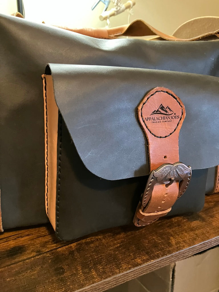 Gray leather bag with brown leather strap and buckle on a wooden surface