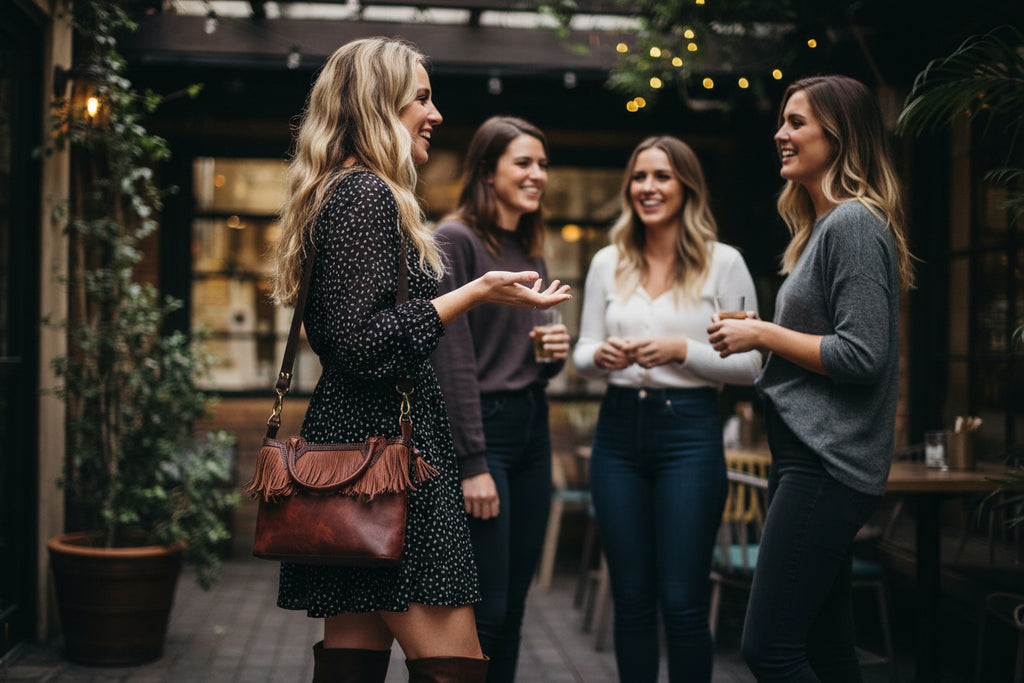 Four women are standing together, engaged in conversation, in an outdoor setting with plants and a casual atmosphere.
