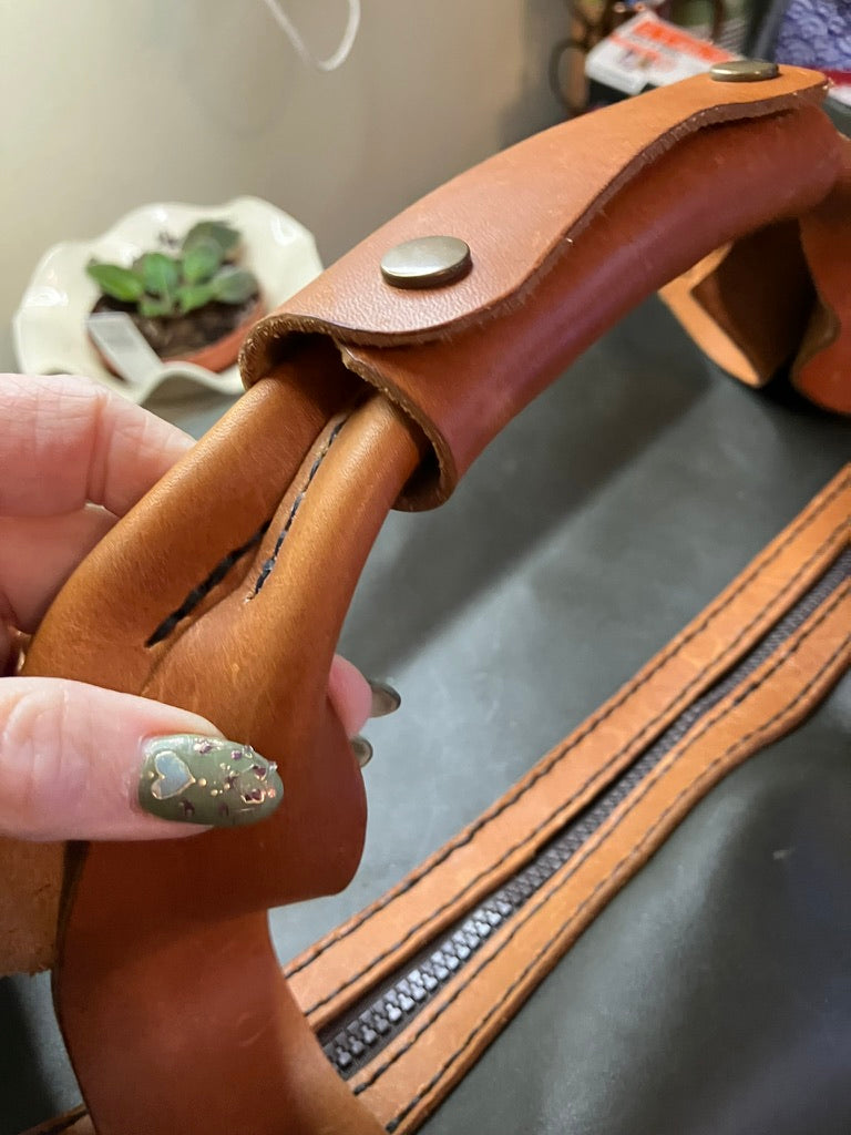 Close-up of a brown leather handle with a button, held by a hand.