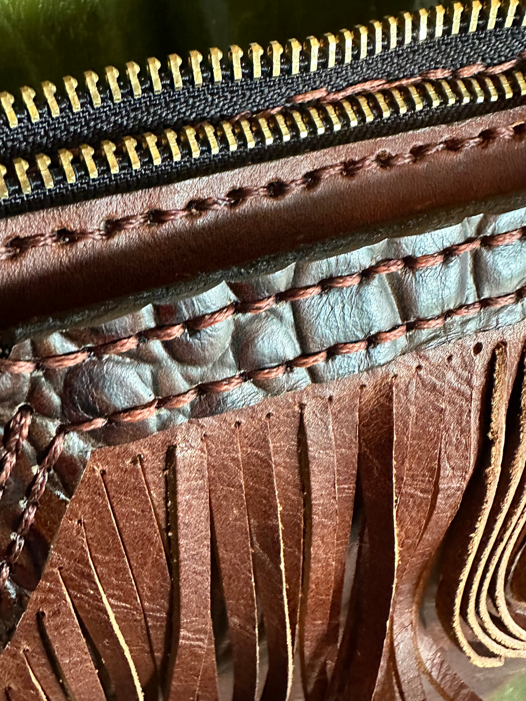 Close-up of a brown leather wallet with gold zipper and stitching details.