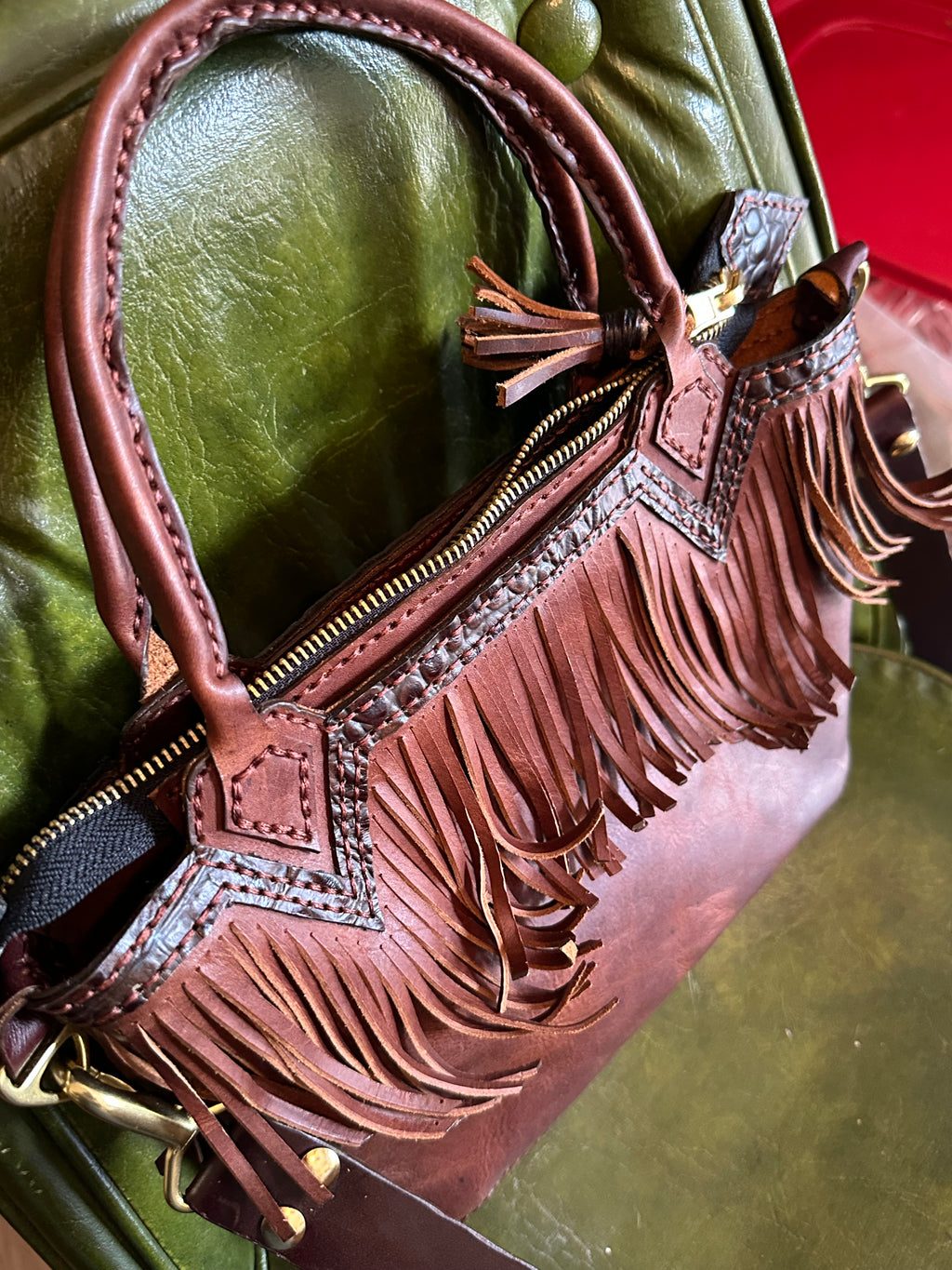 Brown leather handbag with fringe details on a green surface