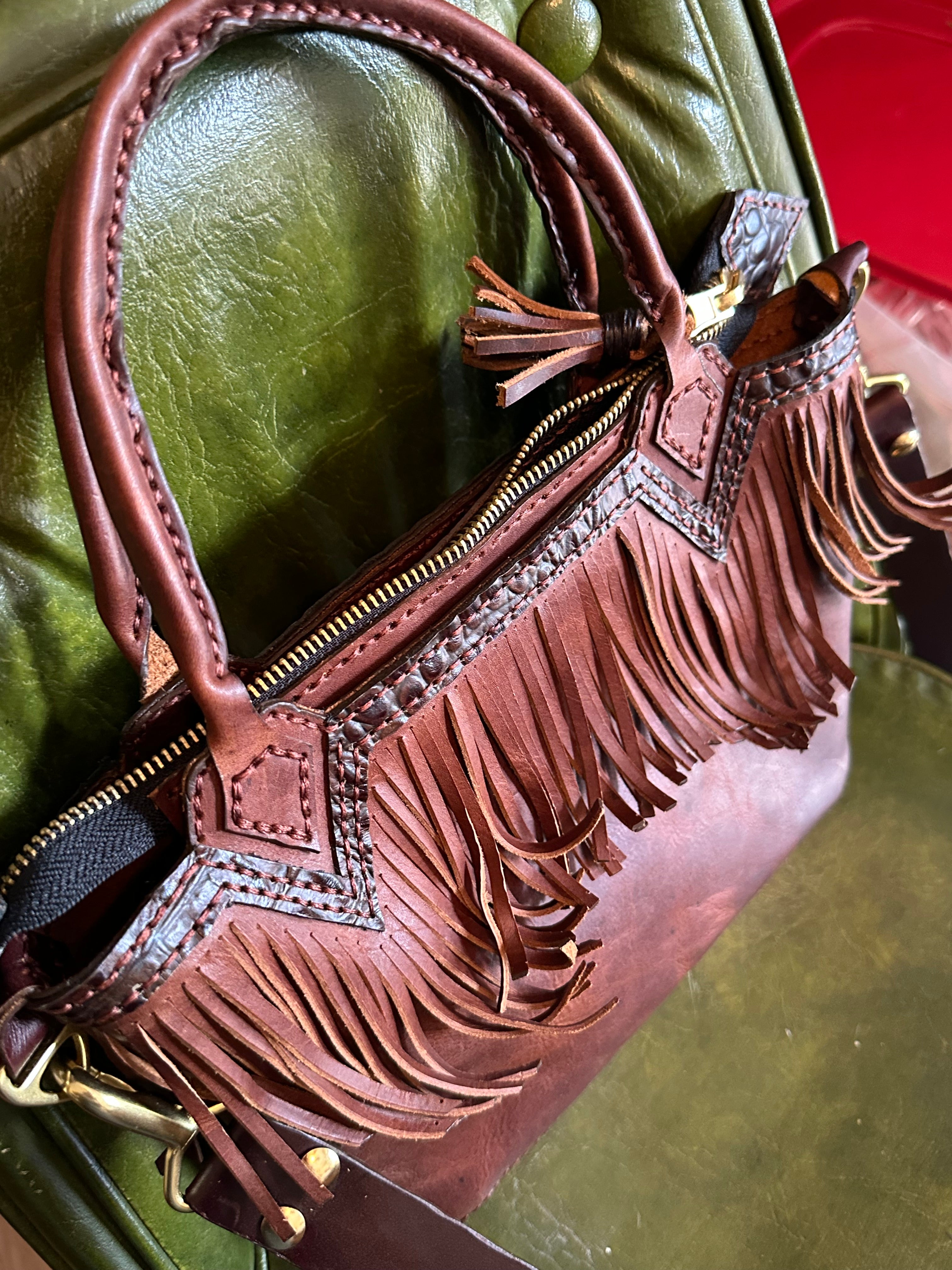 Brown leather handbag with fringe details on a green surface