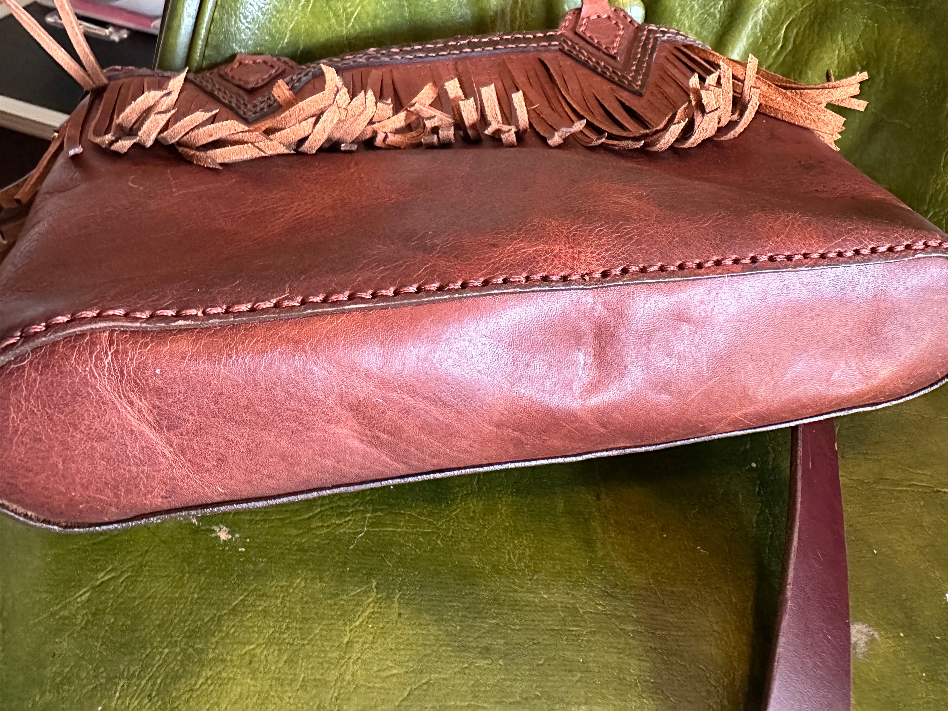 Brown leather handbag with fringe details on a green surface