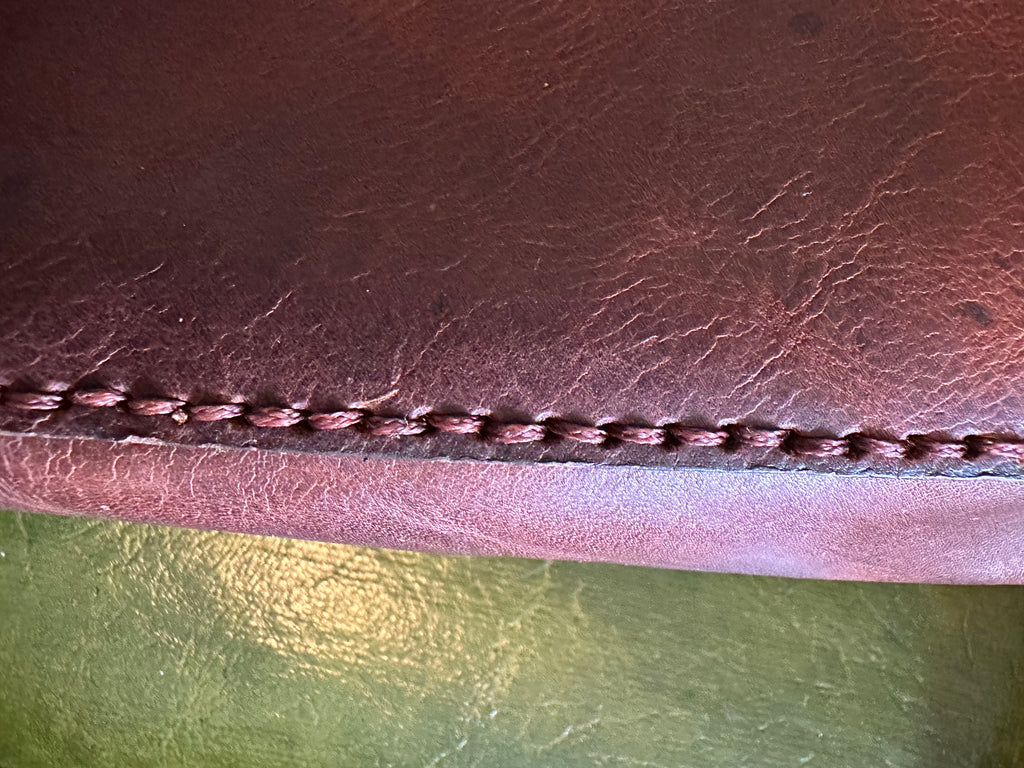 Close-up of brown leather with visible stitching against a green background