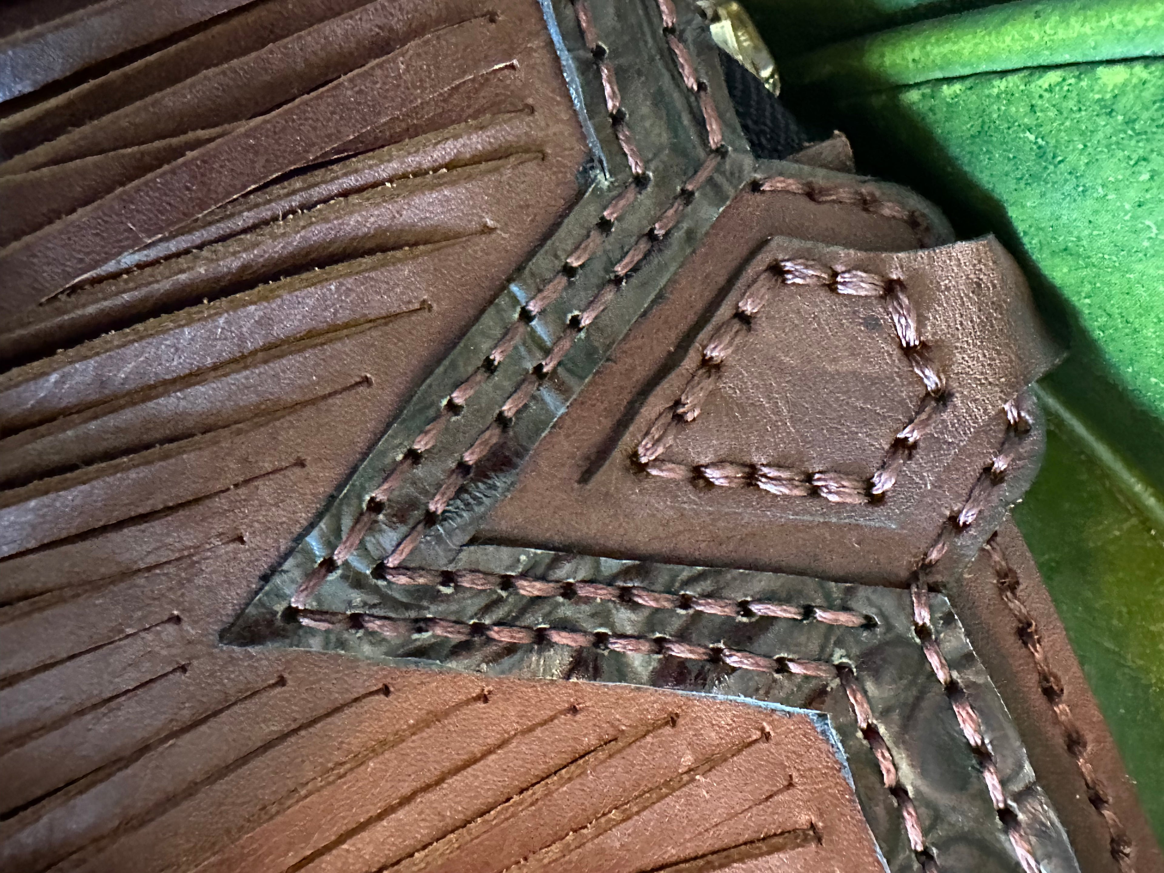 Close-up of brown leather with intricate stitching on a green background