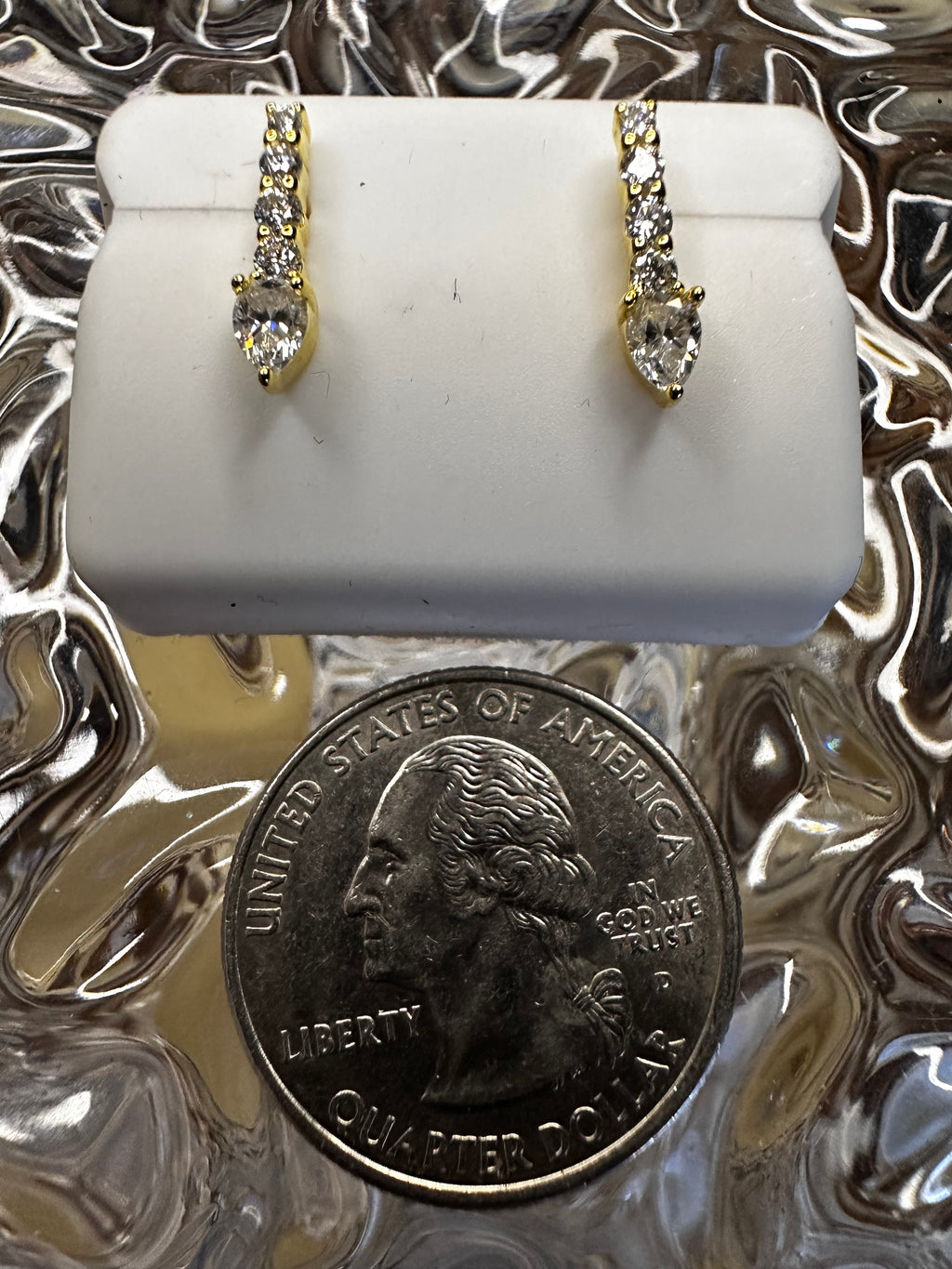 Two diamond rings on a white stand with a quarter for scale against a textured silver background.