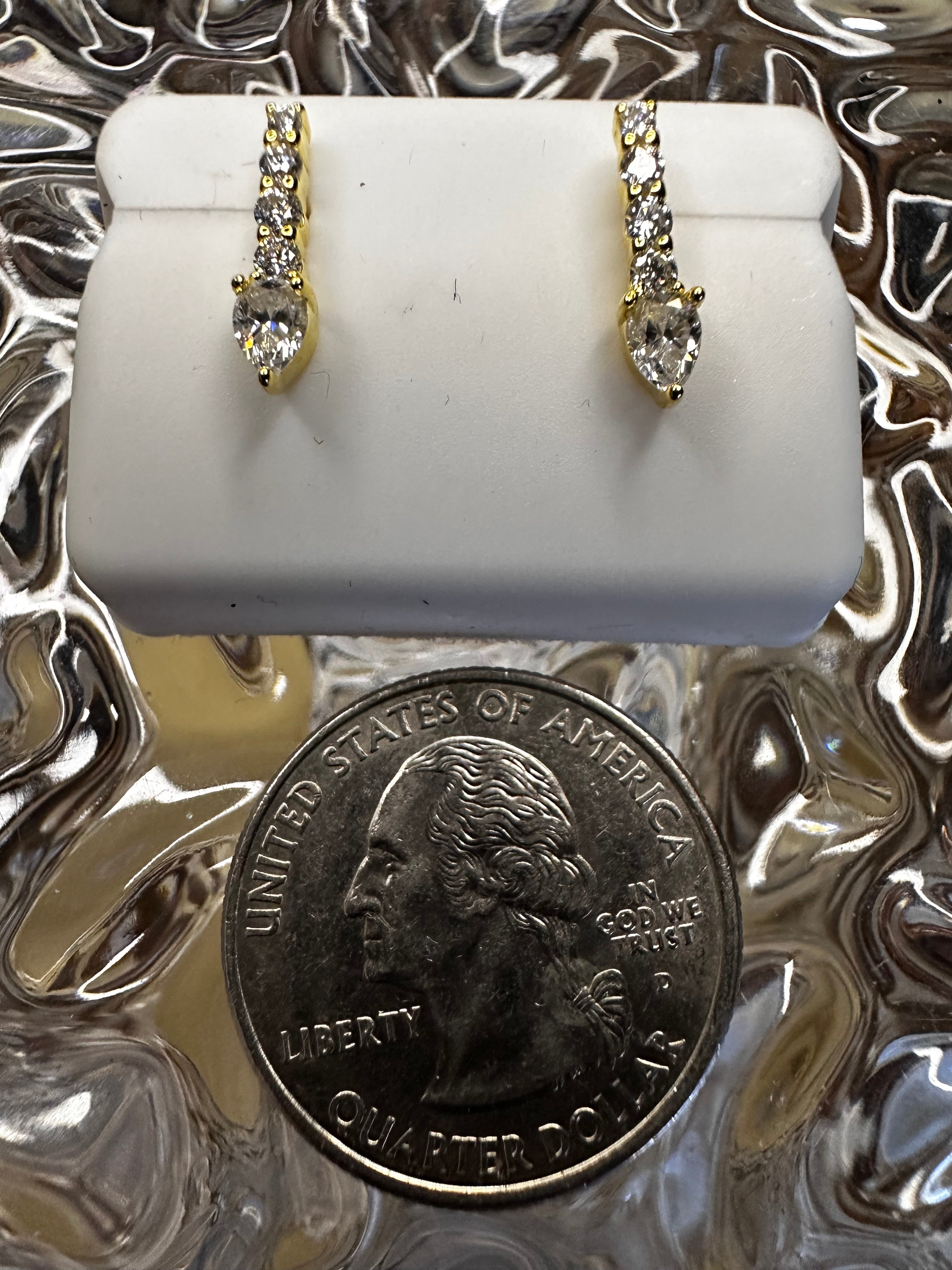 Two diamond rings on a white stand with a quarter for scale against a textured silver background.