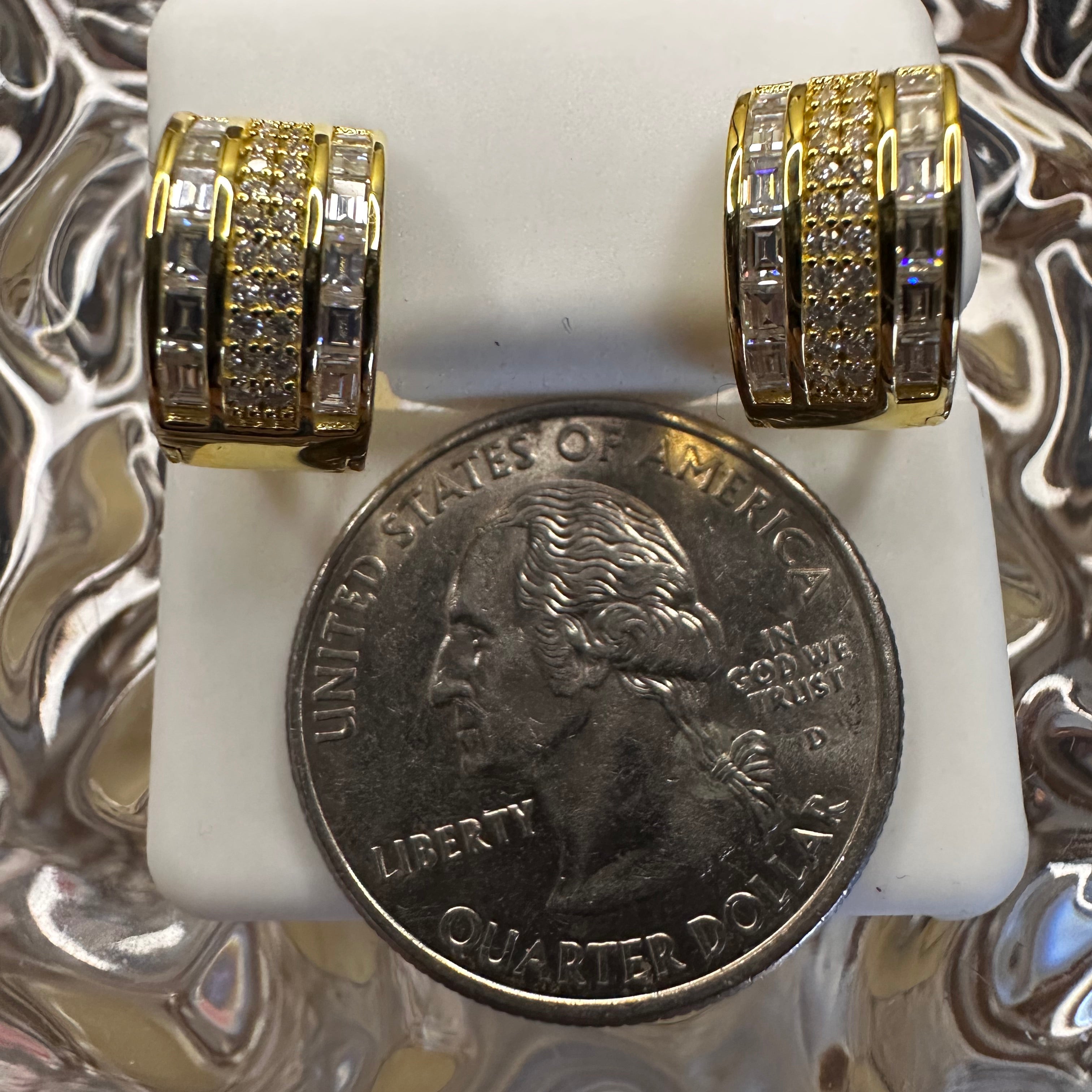 Two gold rings on a white block with a quarter coin for scale against a reflective background
