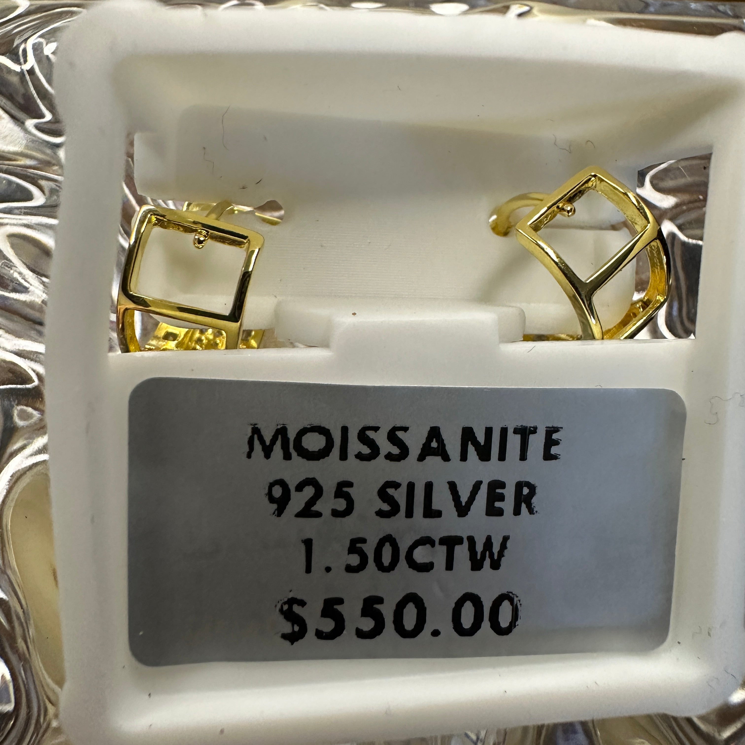 Gold earrings in a display case with a label indicating 'Moissanite', '925 Silver', weight, and price.
