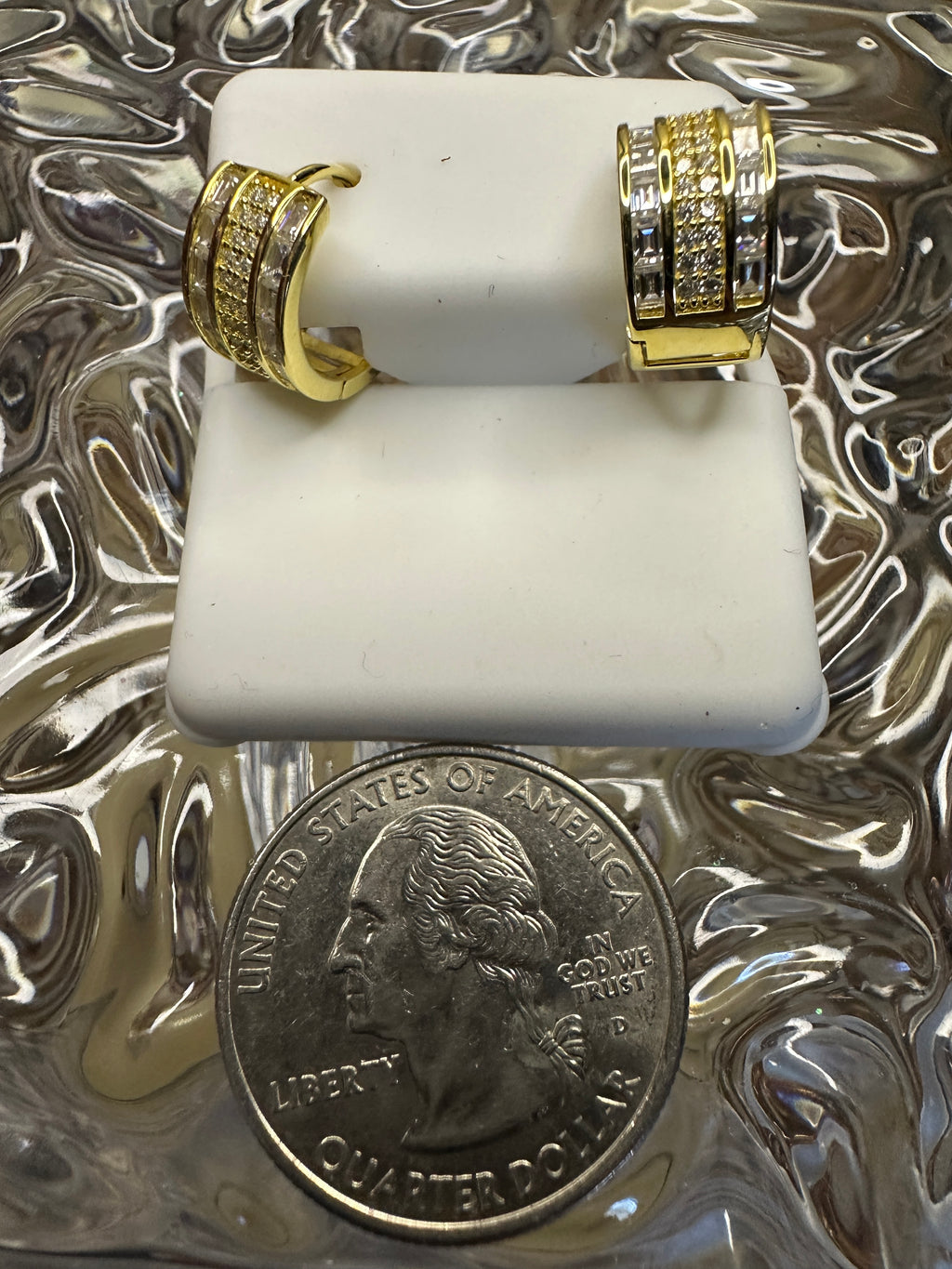 Two gold rings on a white stand with a quarter dollar coin below.