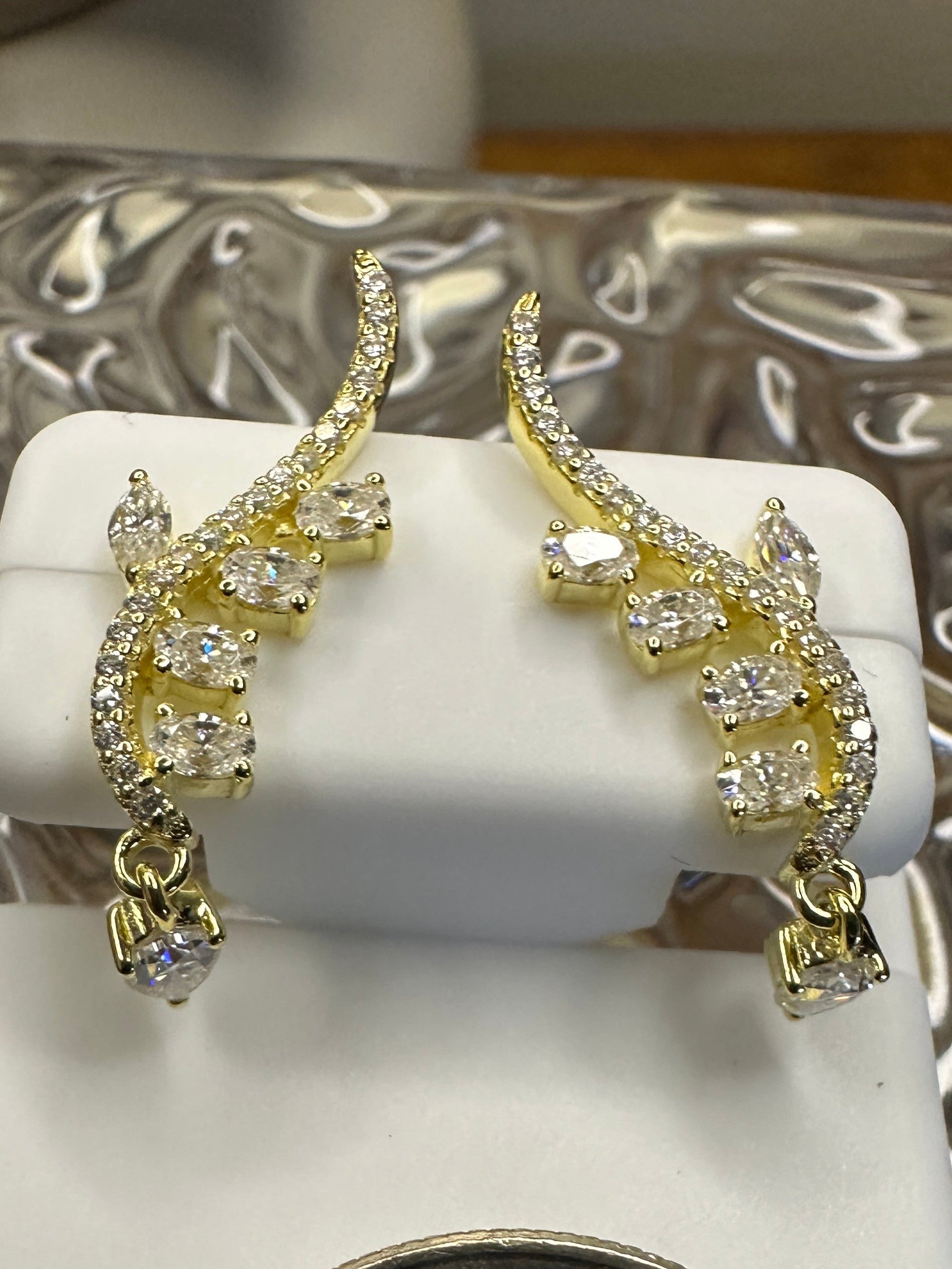 Gold earrings on a white stand with a quarter for scale, against a decorative silver background.