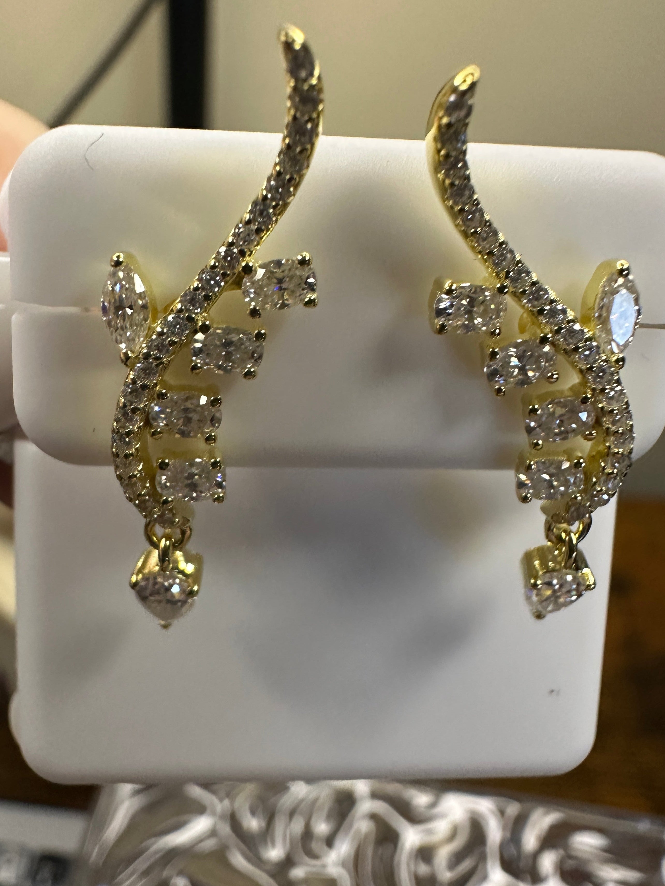 Gold and diamond earrings on a white stand with a blurred background