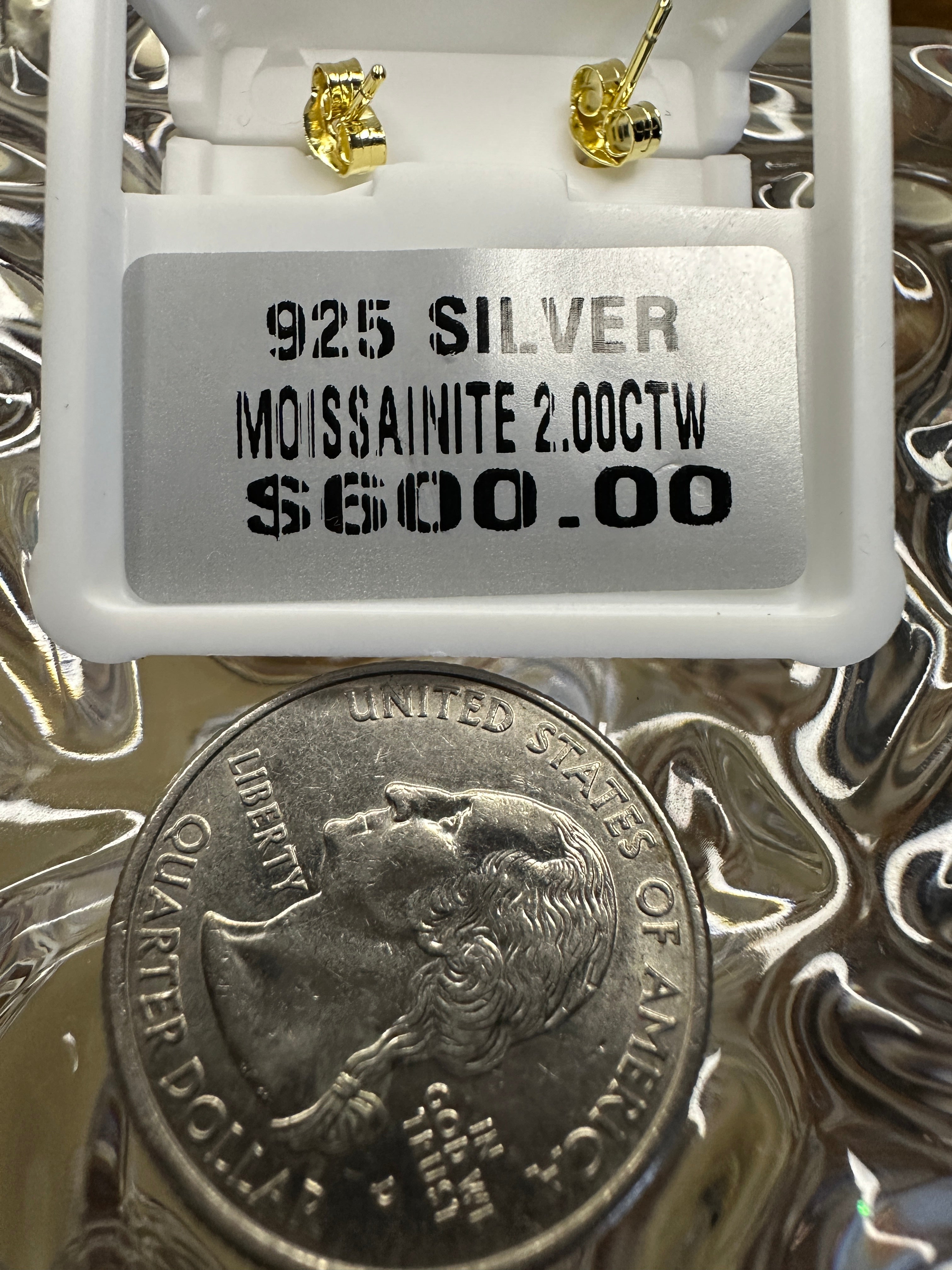 Jewelry display with '925 Silver Moissanite 2.00CTW' label and a quarter coin underneath.