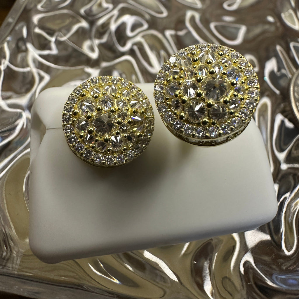Gold and diamond earrings on a white stand with a decorative silver box in the background