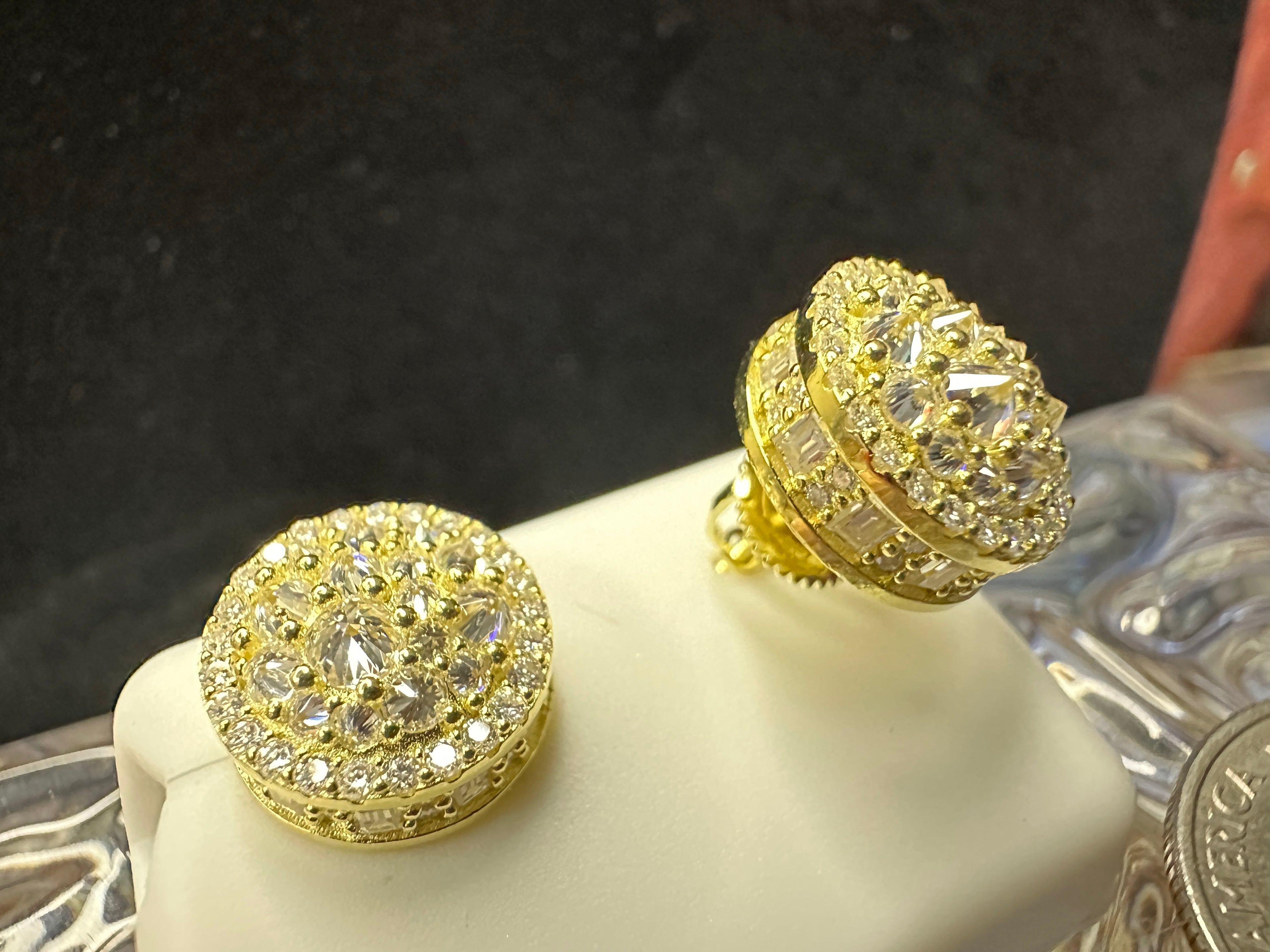 Gold and diamond earrings on a clear stand with a dark background