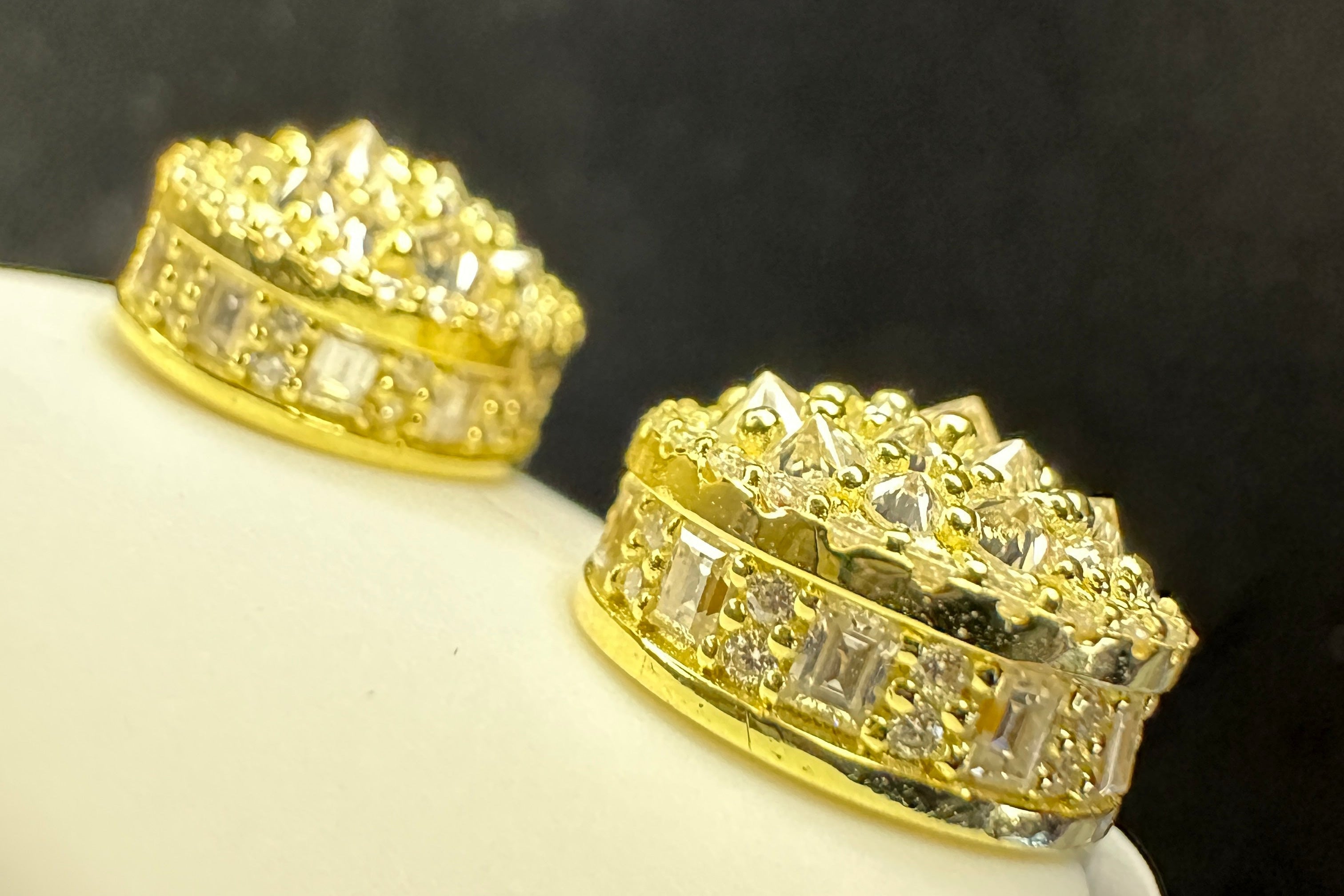 Gold earrings with diamond accents on a white stand against a dark background