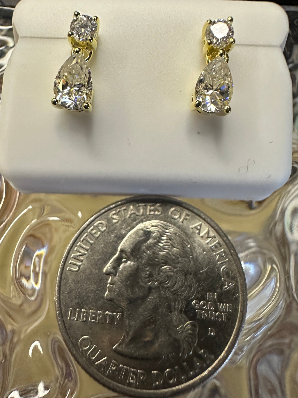 Gold and diamond earrings on a white stand with a quarter for scale.