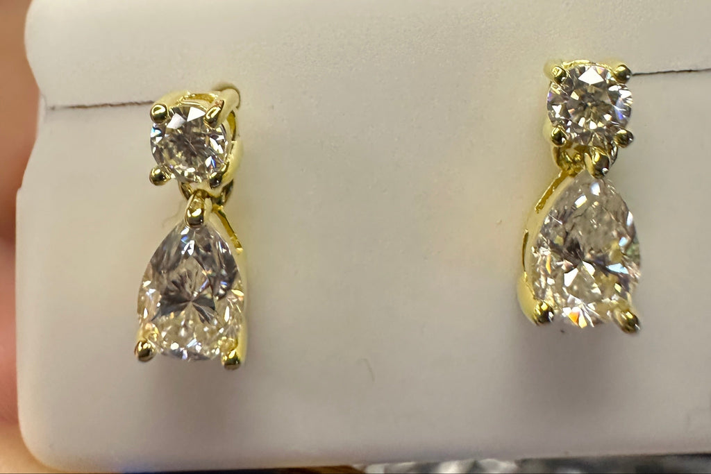 Gold earrings with clear stones on a white stand.