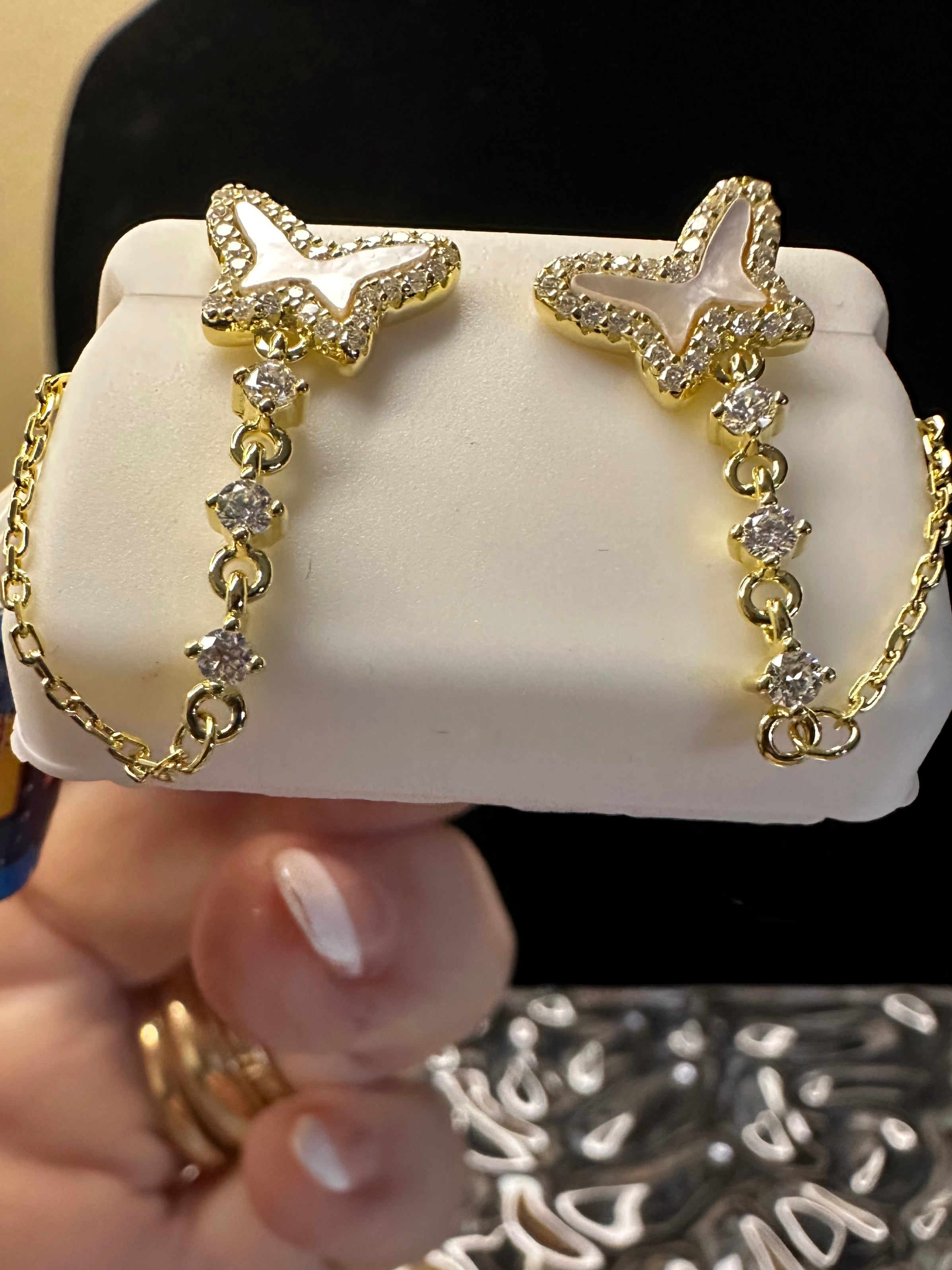 Gold butterfly earrings on a white stand with a hand holding a decorative 