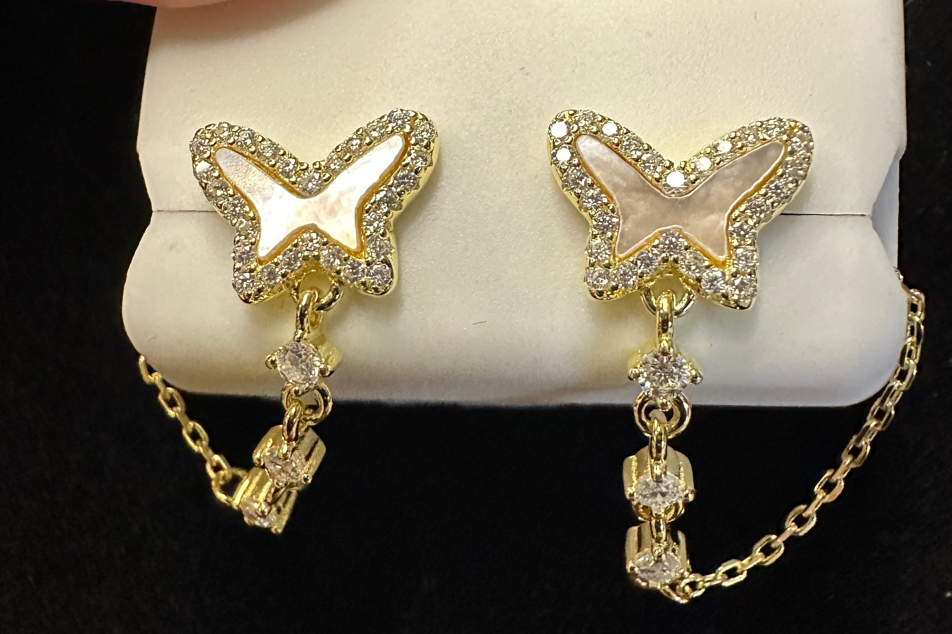 Butterfly-shaped earrings with gold chains on a white jewelry box against a black background.