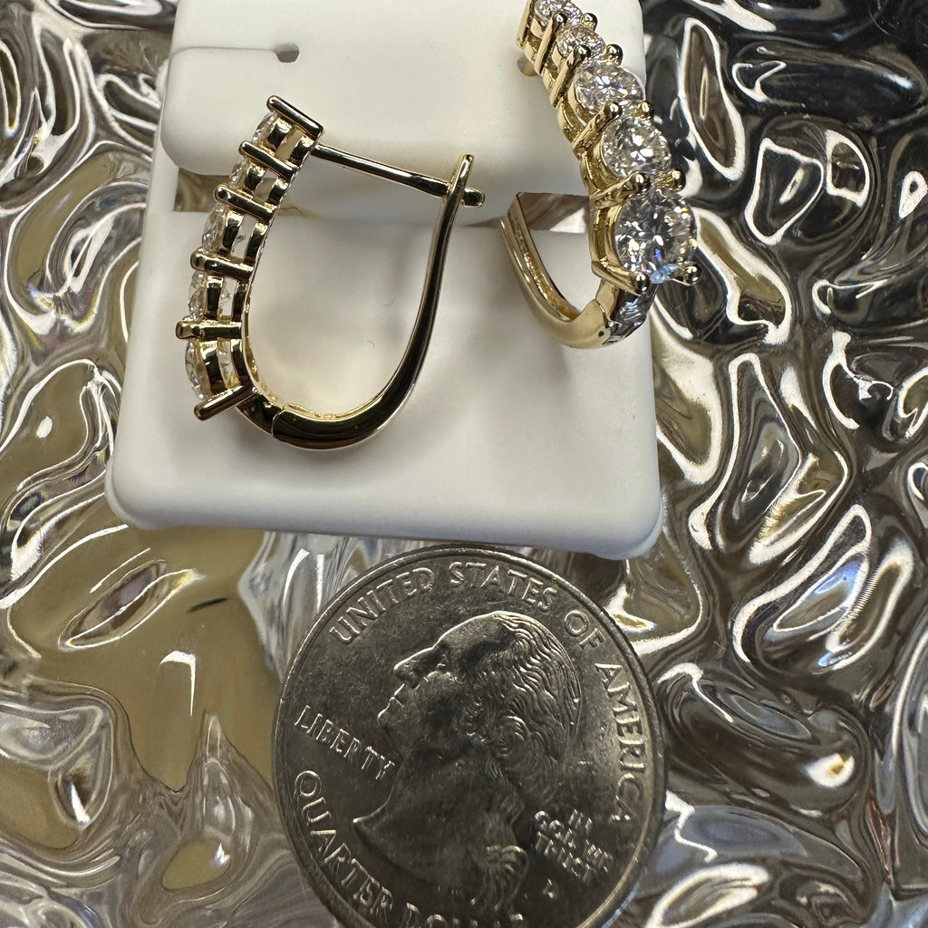 Gold hoop earrings on a white stand with a quarter for scale, on a reflective surface.