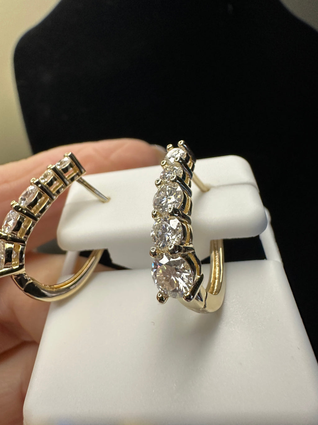 Gold hoop earrings with clear gemstones on a white stand.