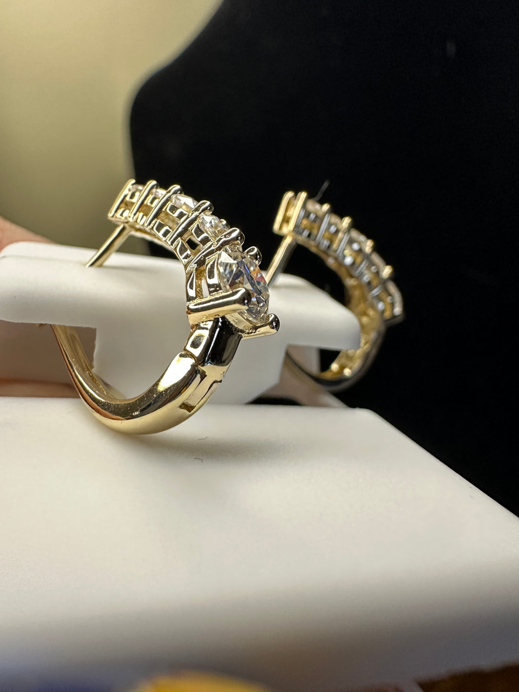 Gold hoop earrings with clear gemstones on a white stand.