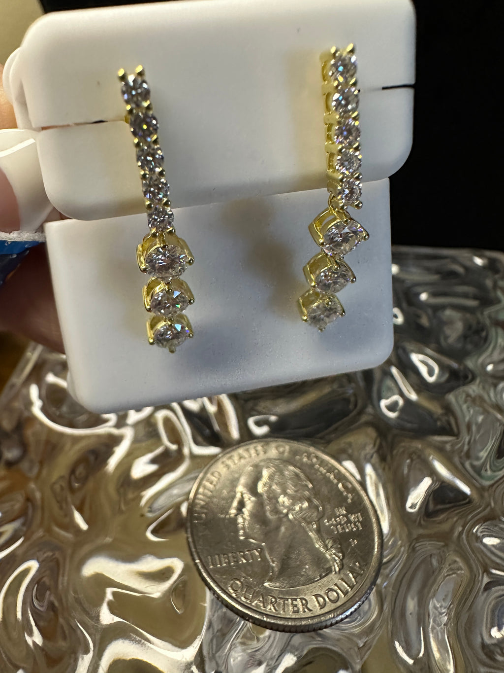 Gold earrings displayed on a white stand with a quarter for scale.