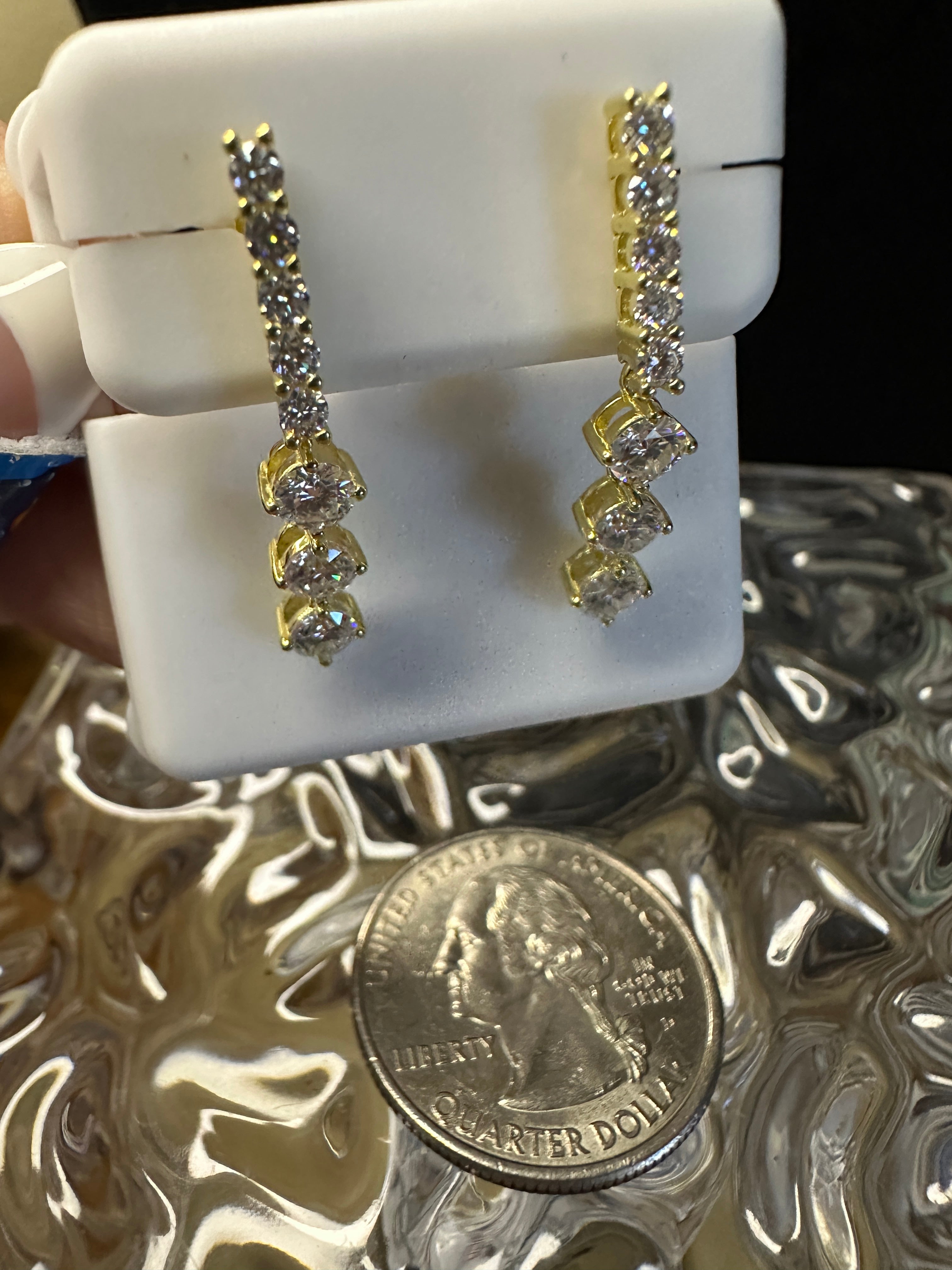 Gold earrings displayed on a white stand with a quarter for scale.