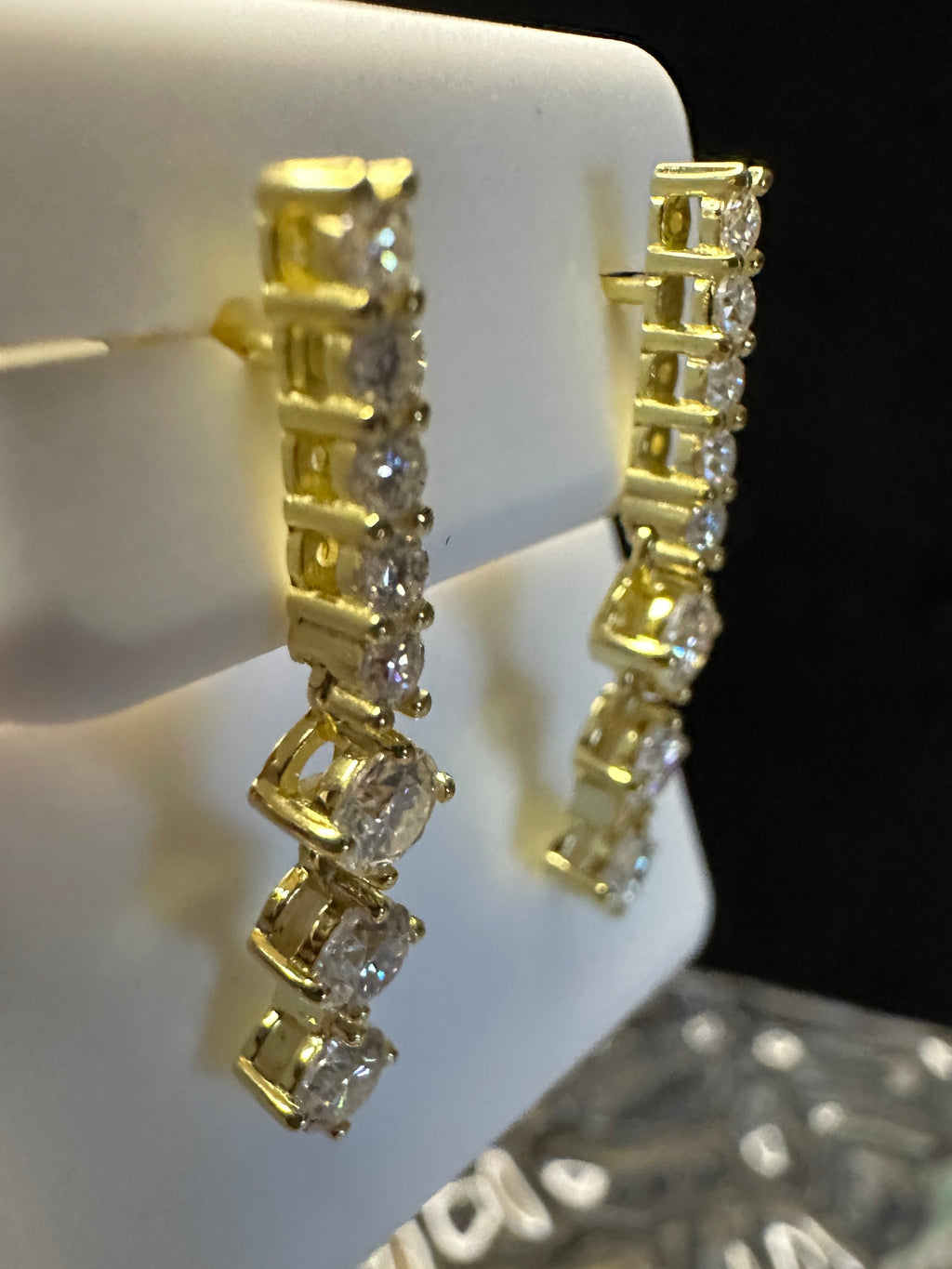 Gold post tennis earrings with diamond accents on a white stand.