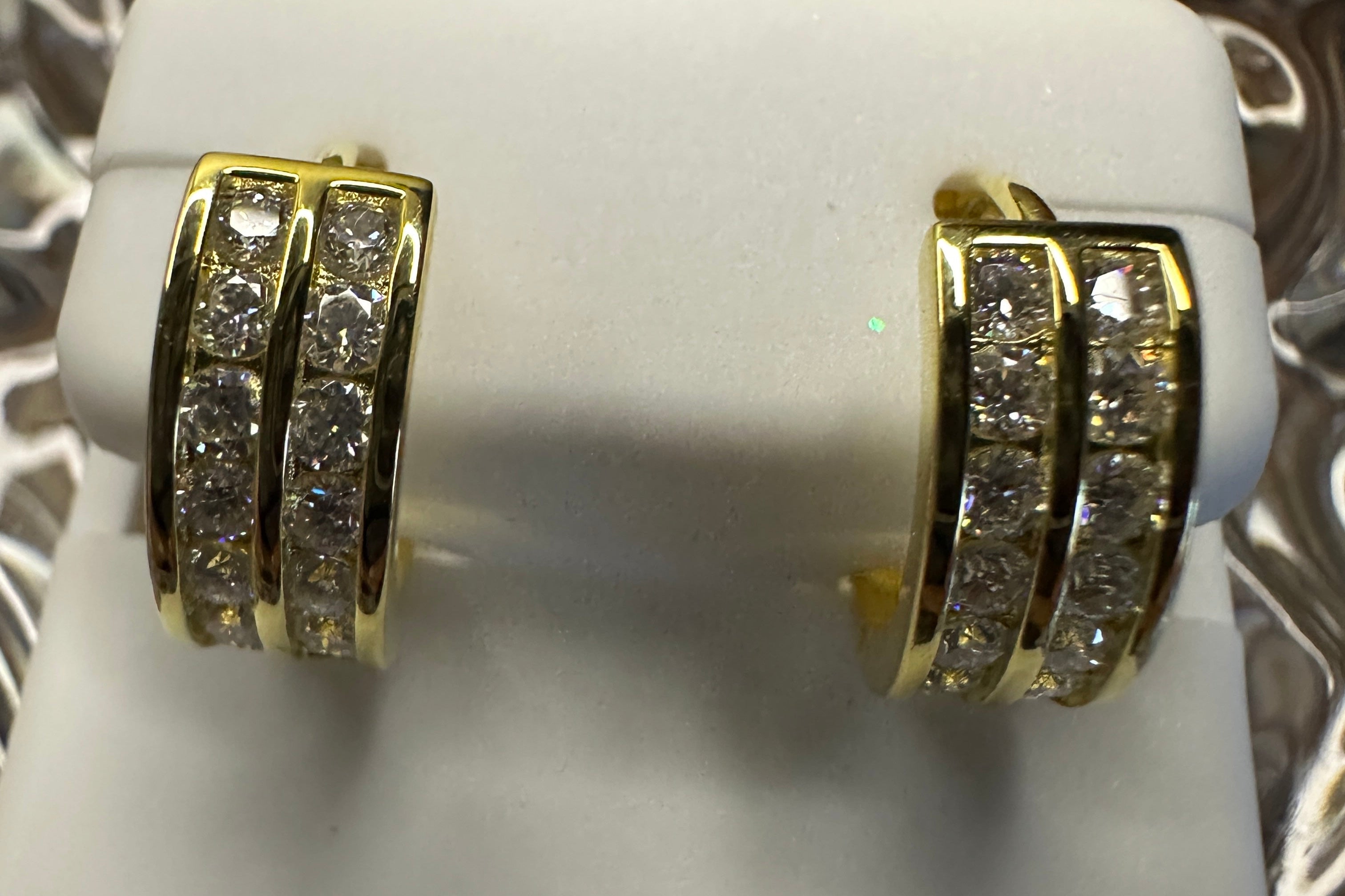 Gold hoop earrings with embedded stones on a white stand.