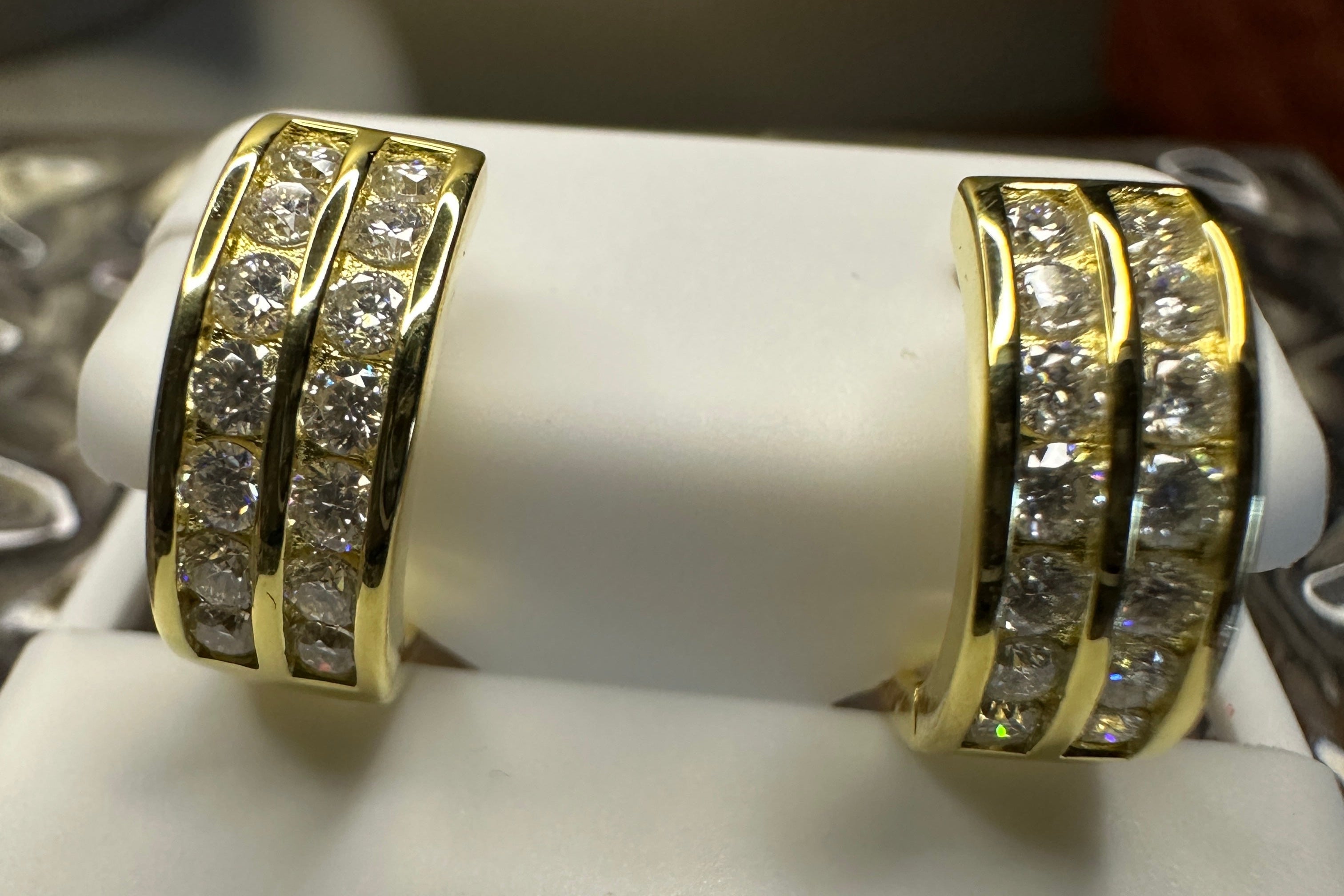 Gold hoop earrings with diamond accents on a white stand.