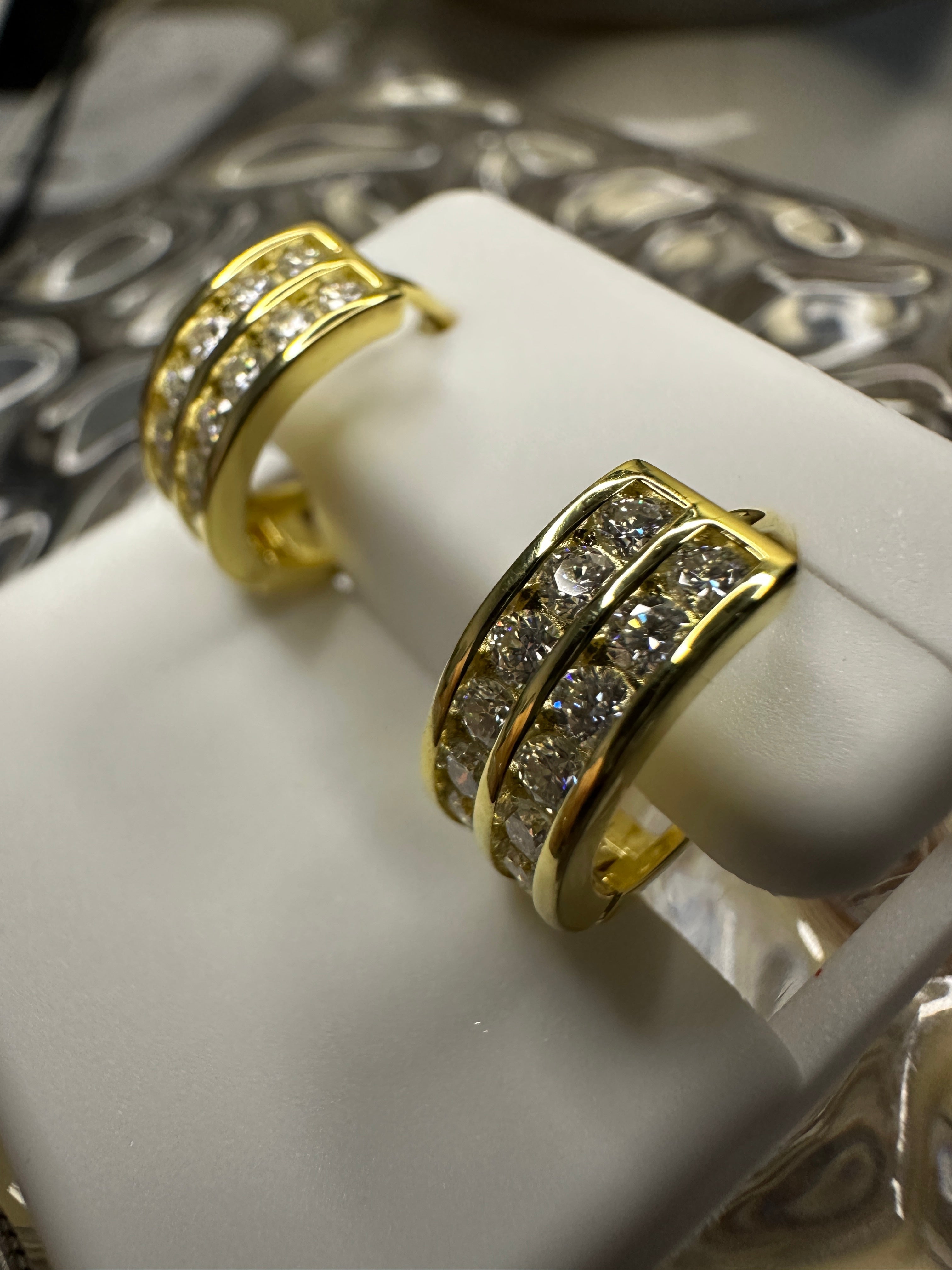 Gold hoop earrings with diamond accents on a white stand.