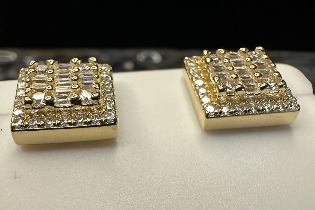 Pair of gold square earrings with gemstones on a white surface.