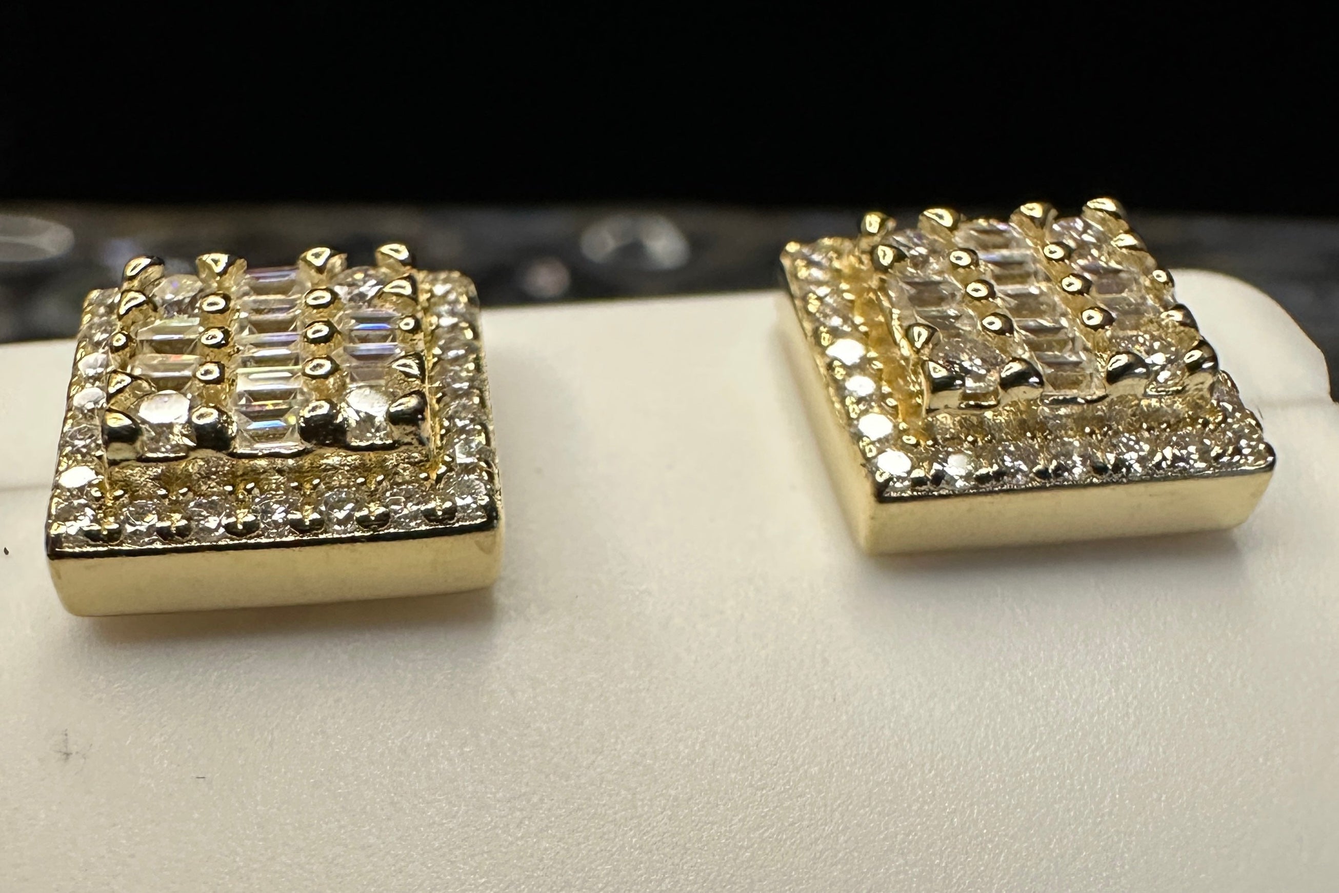 Pair of gold square earrings with gemstones on a white surface.