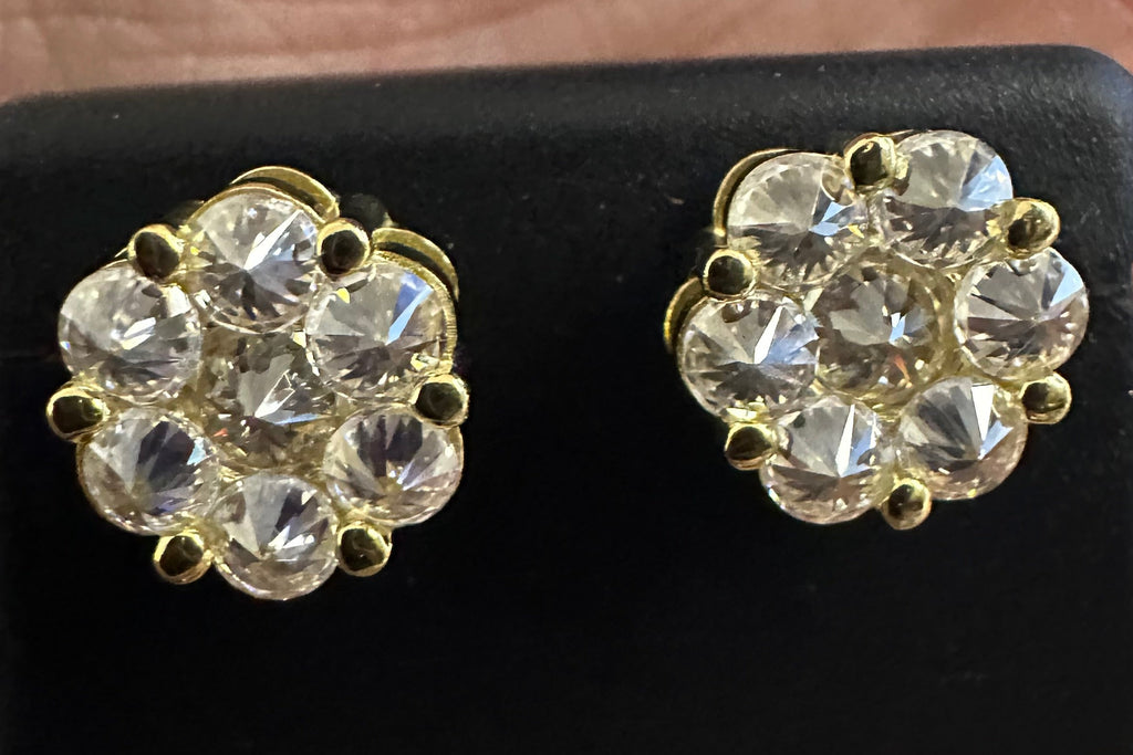 Gold and crystal earrings on a black stand held between fingers.