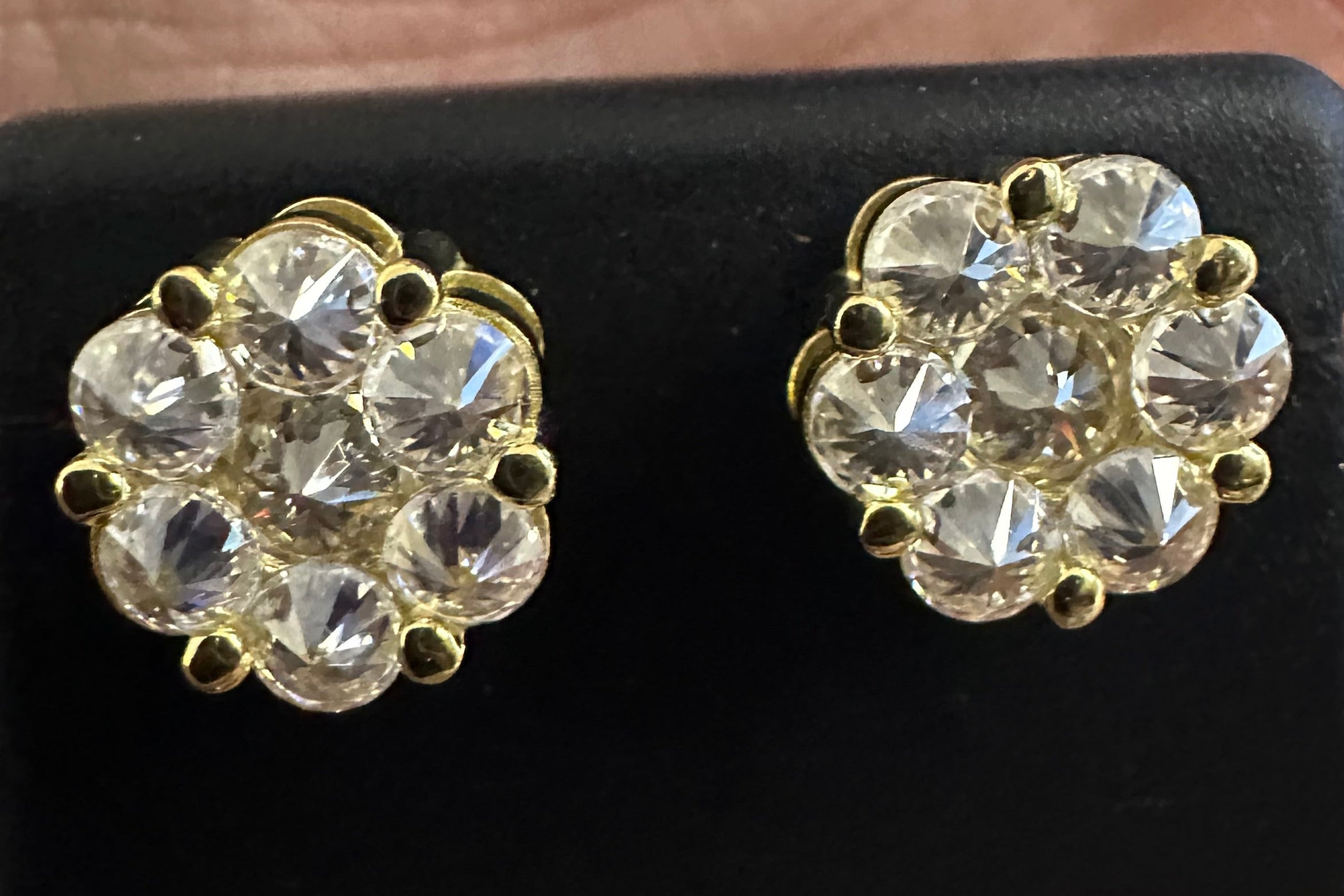 Gold and crystal earrings on a black stand held between fingers.