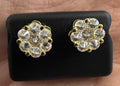 Gold earrings with clear stones on a black display card held in a hand.