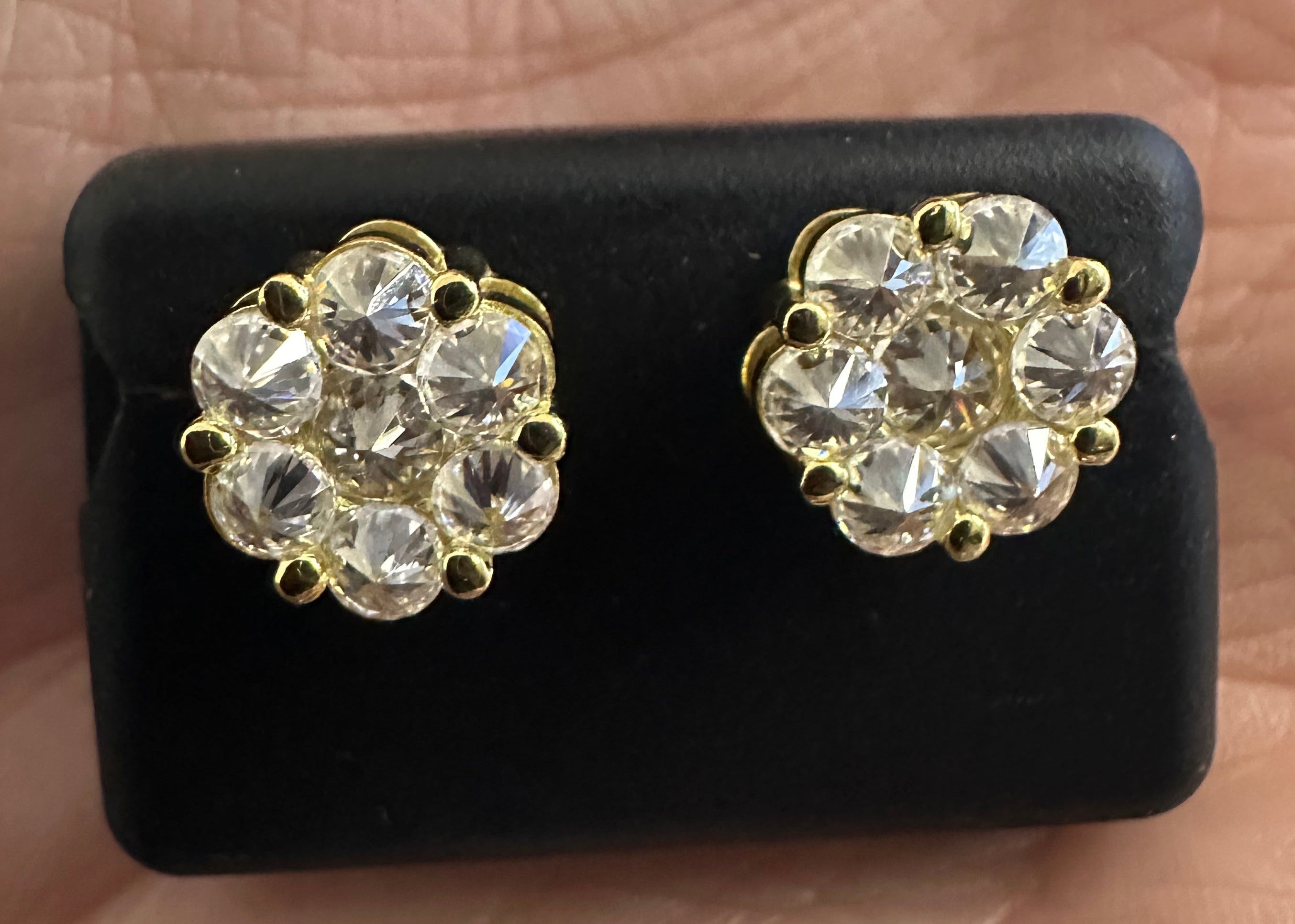 Gold earrings with clear stones on a black display card held in a hand.