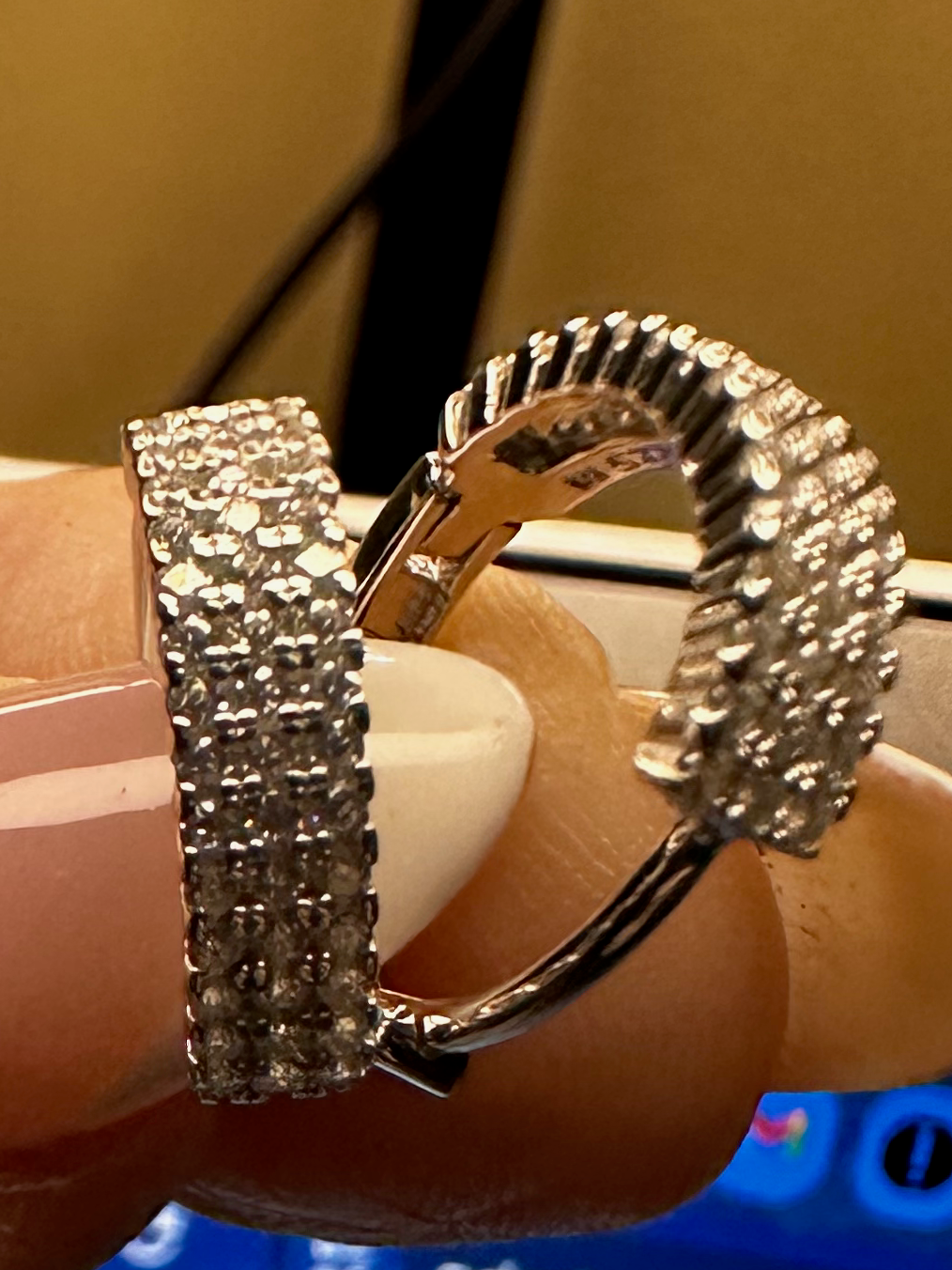 Hand holding a silver ring with intricate design in front of a computer screen displaying Shopify.