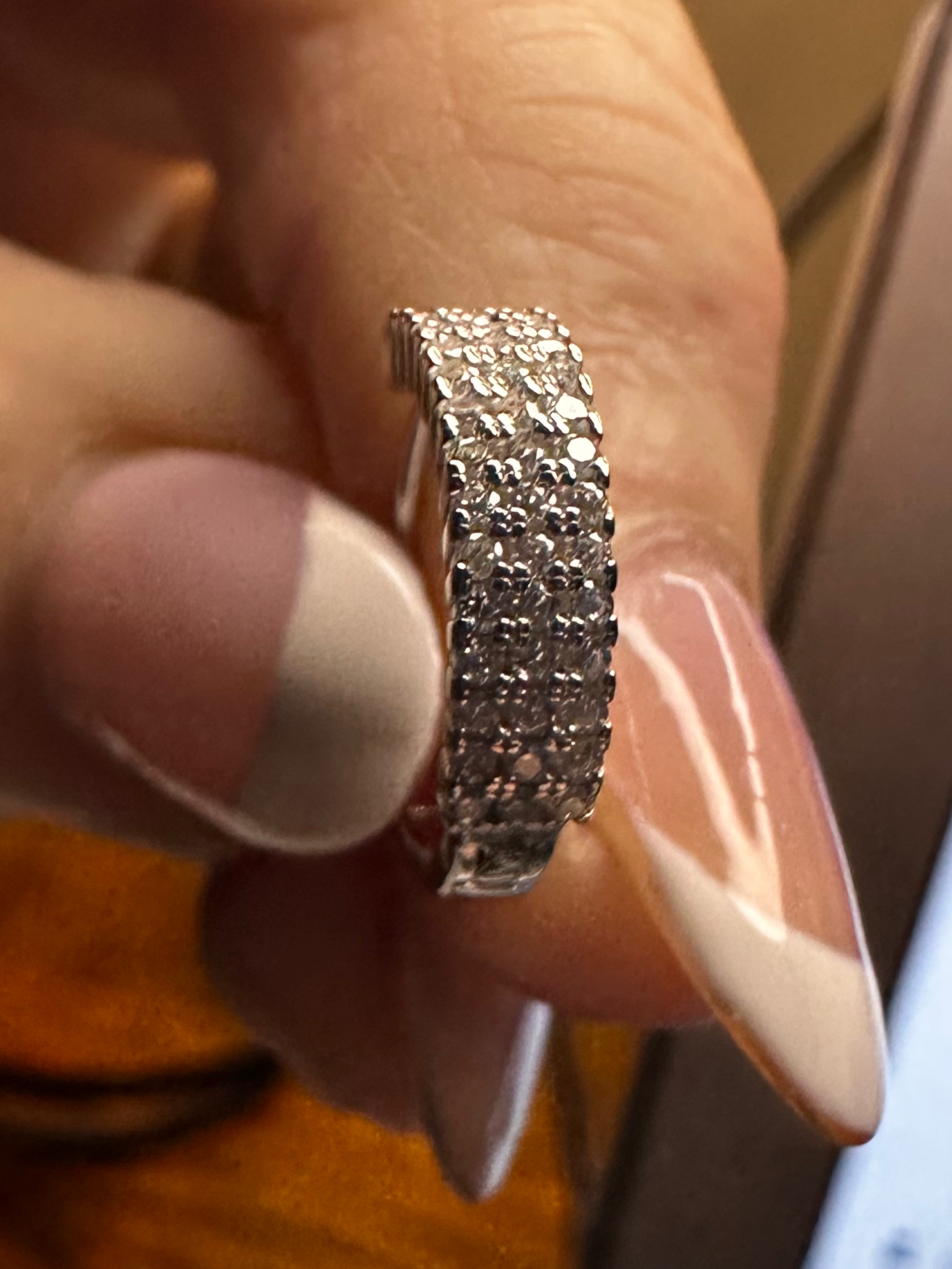 Hand holding a silver ring with a blurred background of a phone and paper.