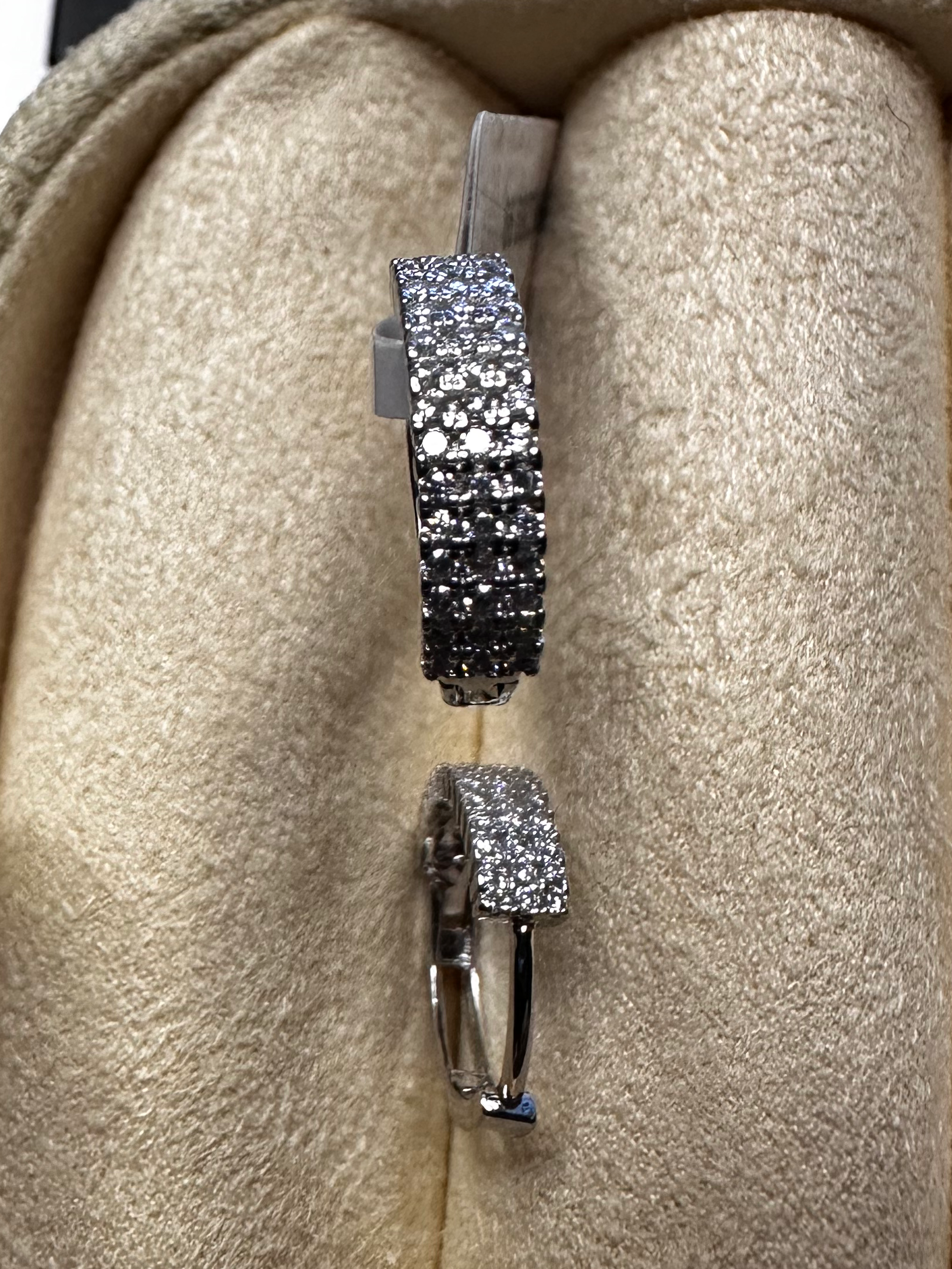 Pair of silver earrings with black and clear gemstones on a beige cushion.