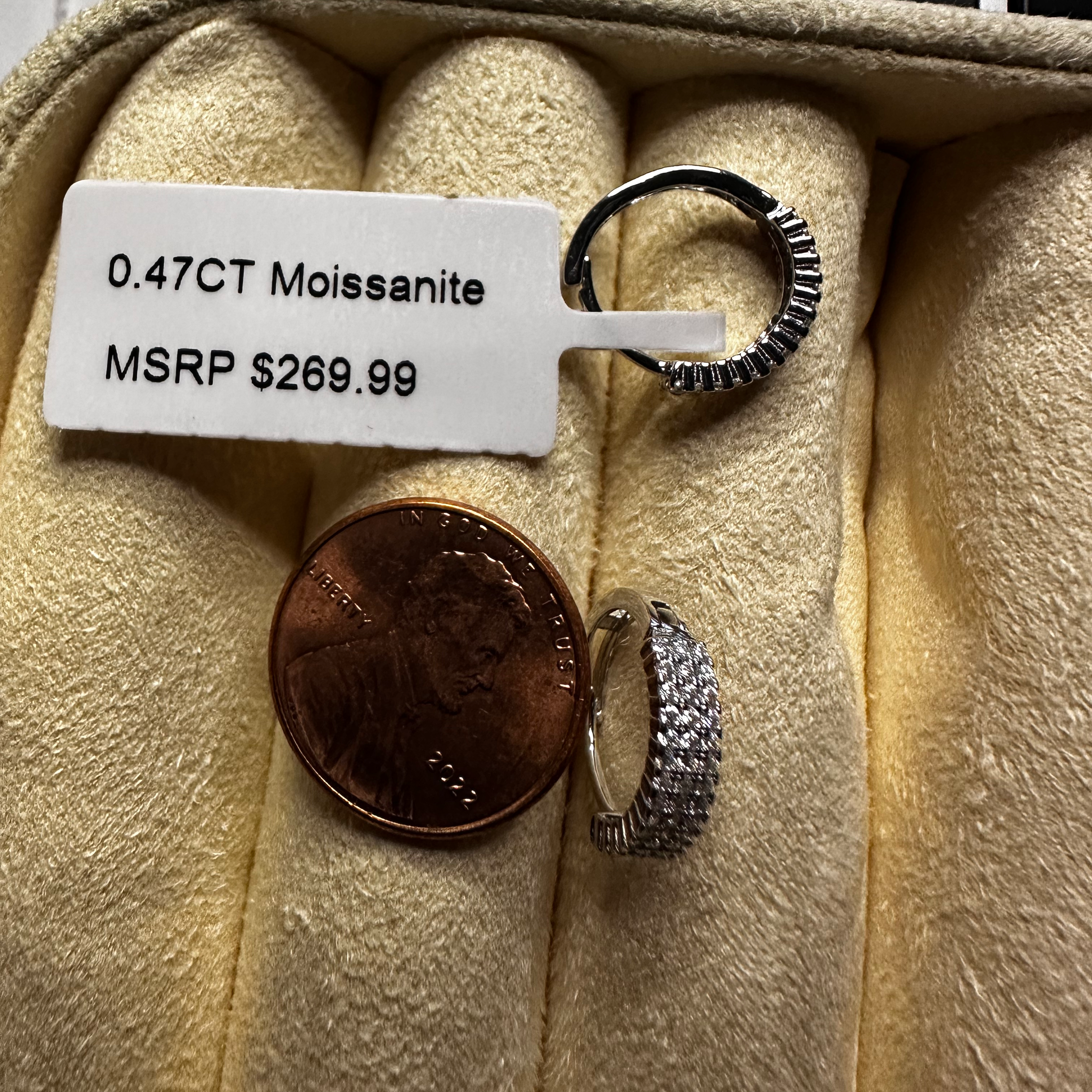 Small diamond ring with a price tag and penny for scale on beige fabric
