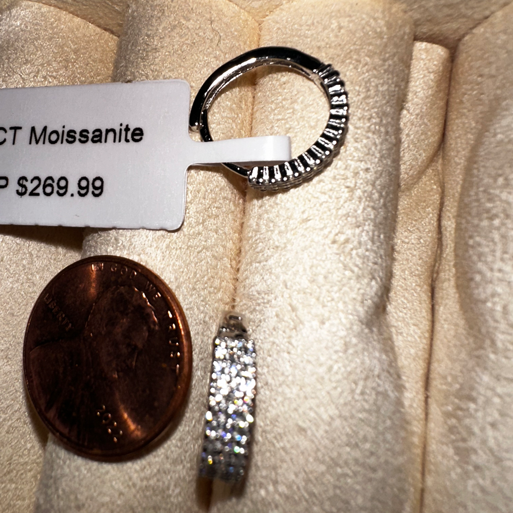 Silver ring with Moissanite stones next to a penny on a textured surface.