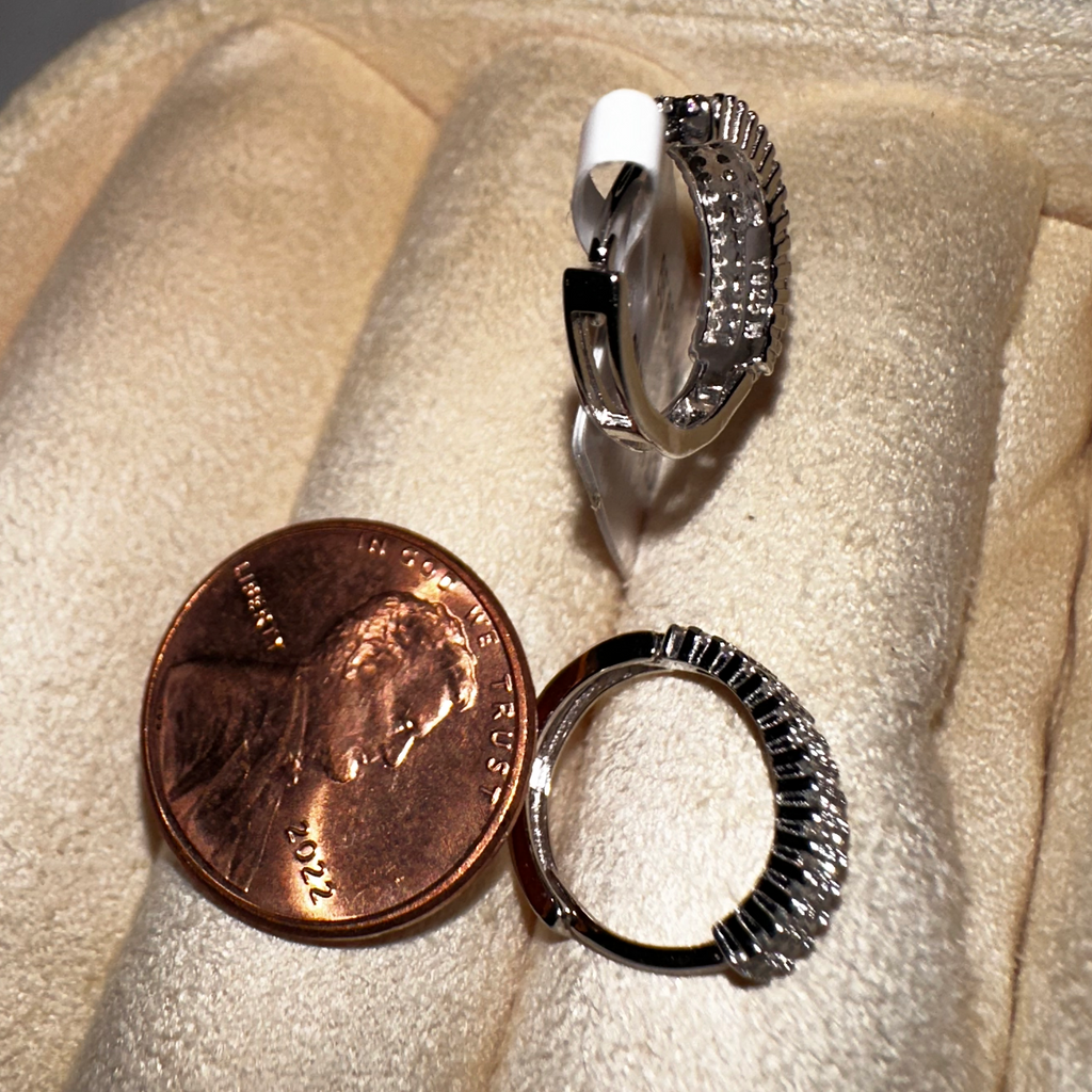 Two silver hoop earrings on a beige surface with a penny for scale.