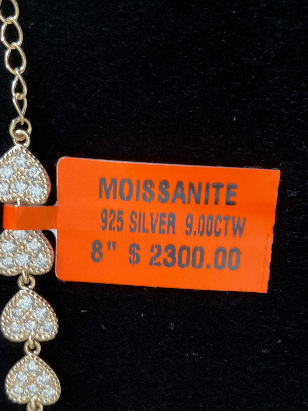 Necklace with heart-shaped pendants and an orange tag displaying product details on a black background
